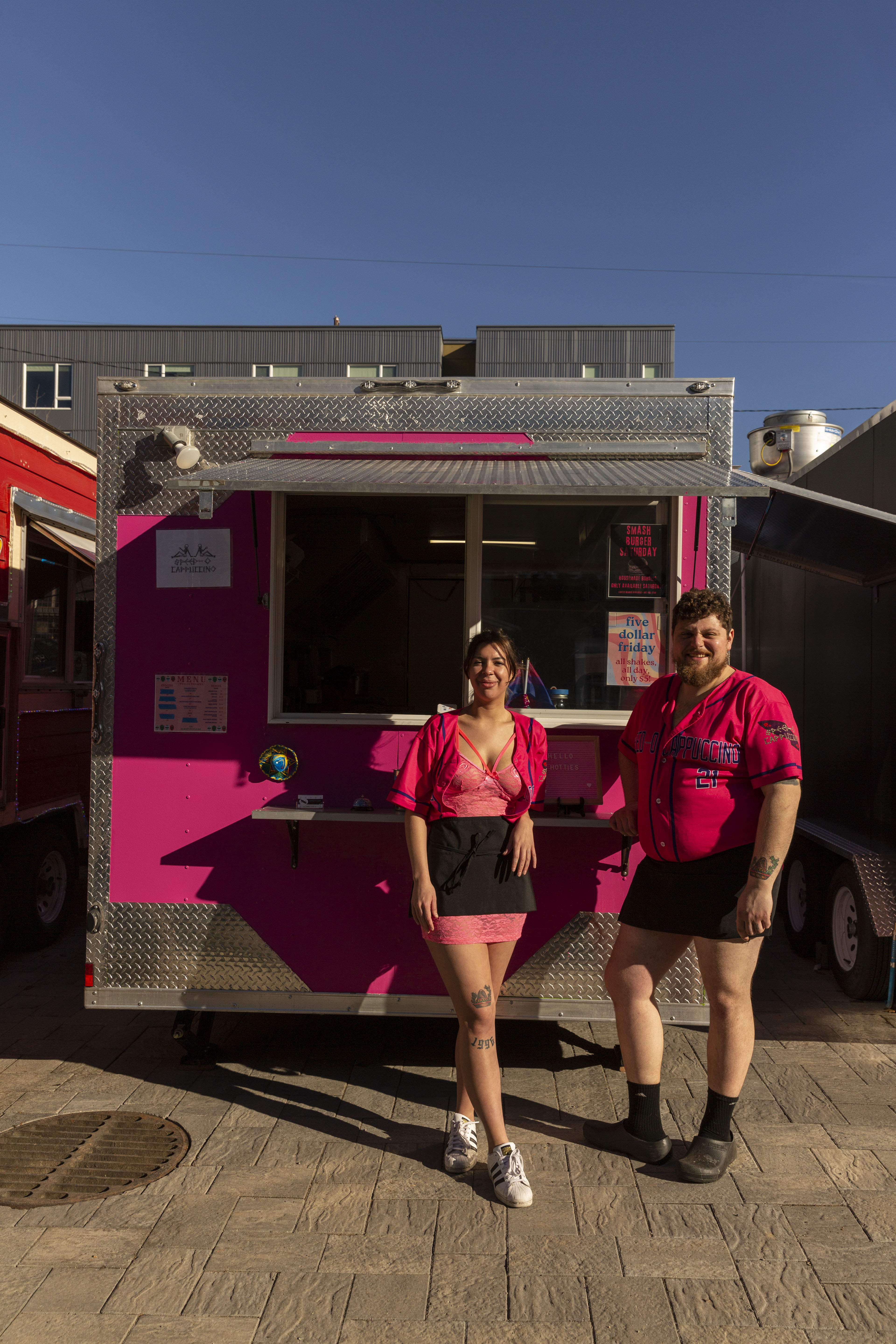 Two people in pink outfits and aprons stand in front of a hot pink cart.