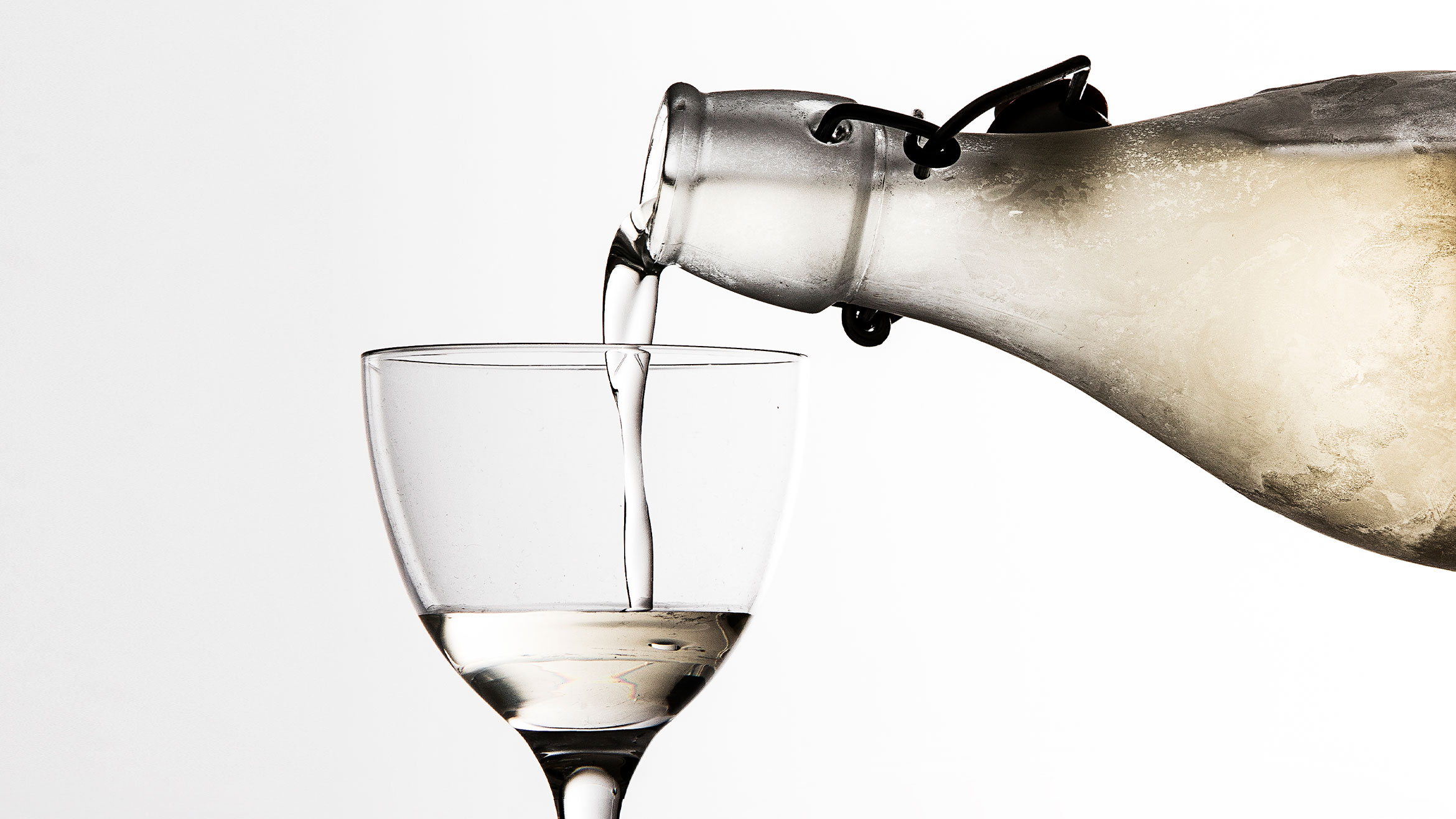 A frosty bottle pours liquid into a cocktail glass
