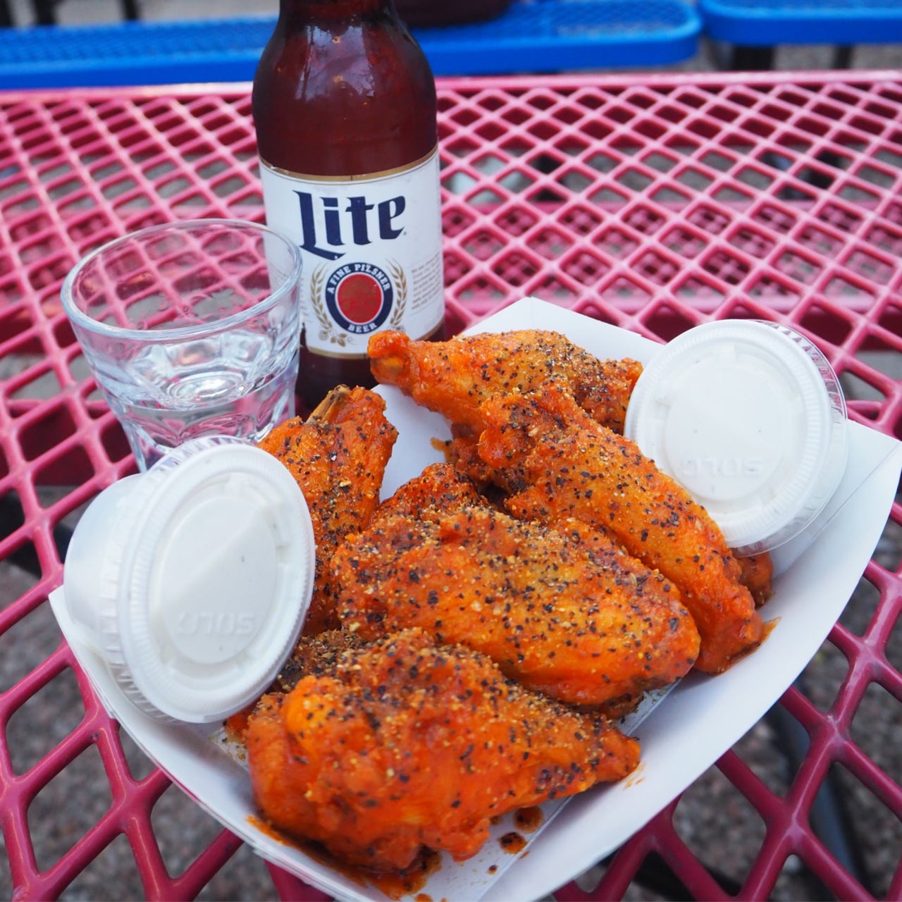 A plate of chicken wings on an outdoor pink-wire table.