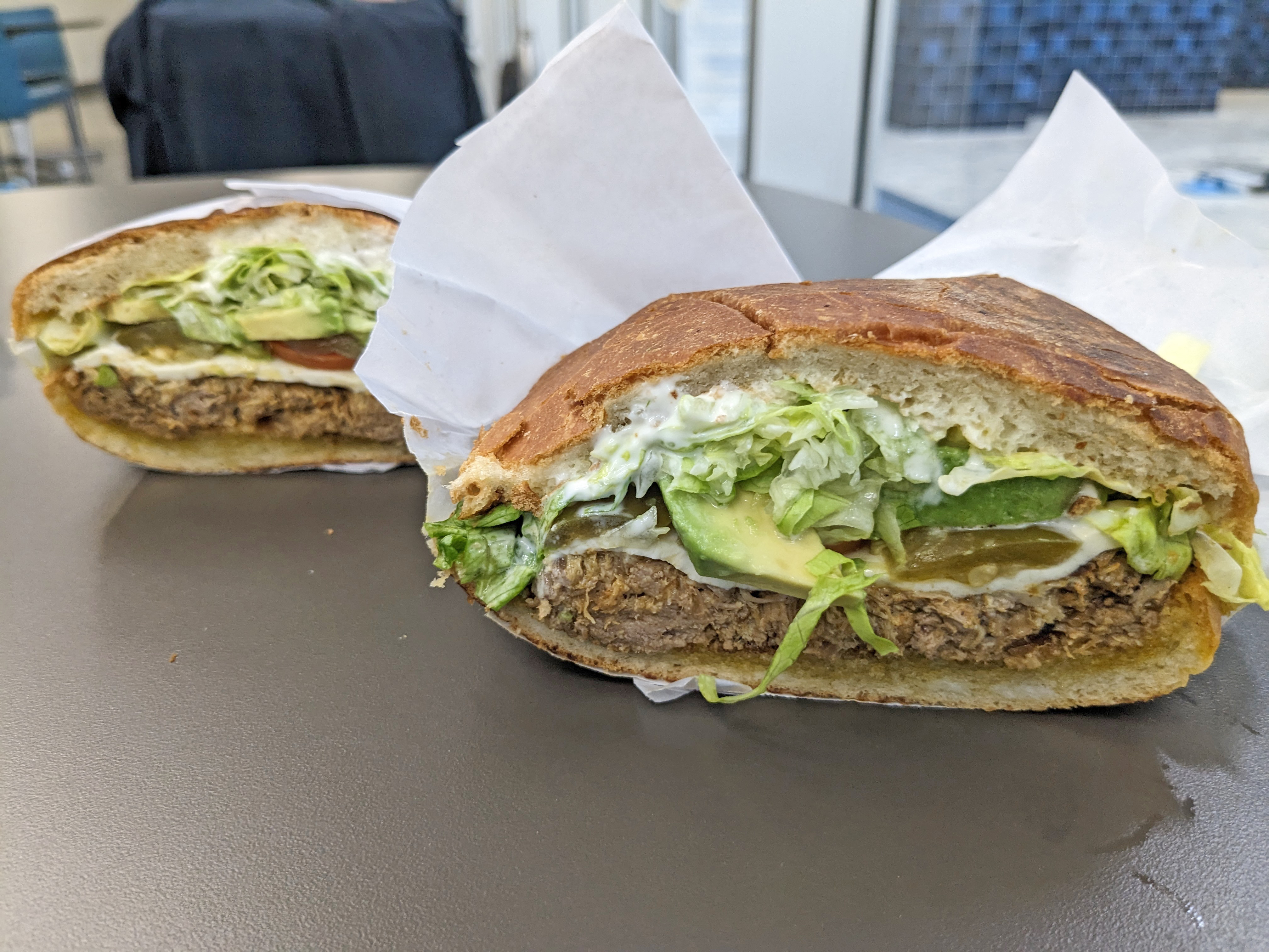 A domed sandwich cut in half revealing meat, avocado, and lettuce.