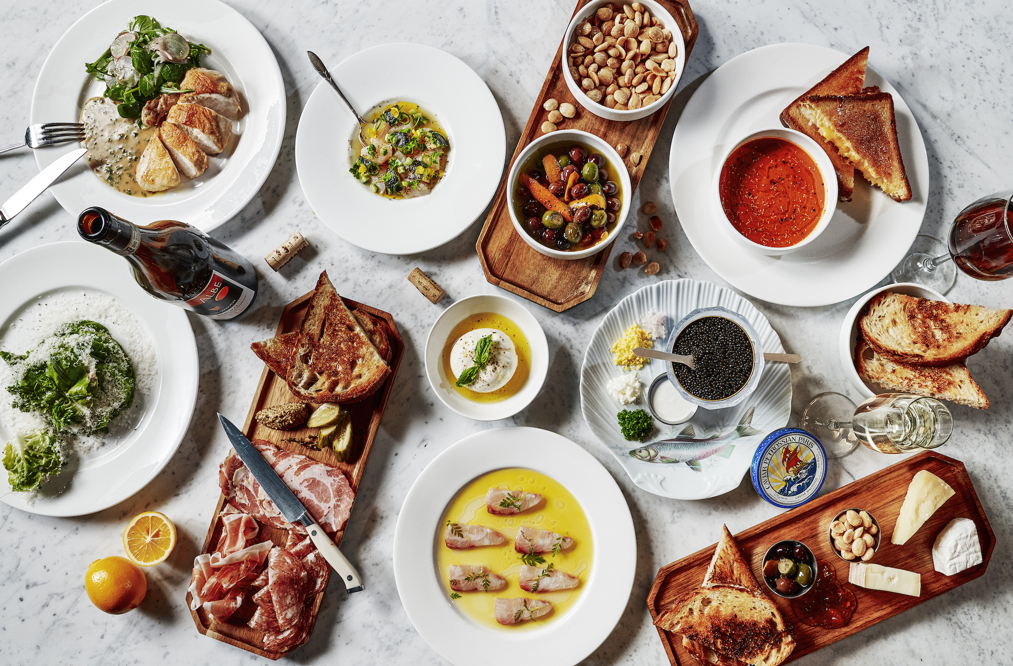 An overhead shot of a crowded marble bar with charcuterie boards, roasted chicken, and more.