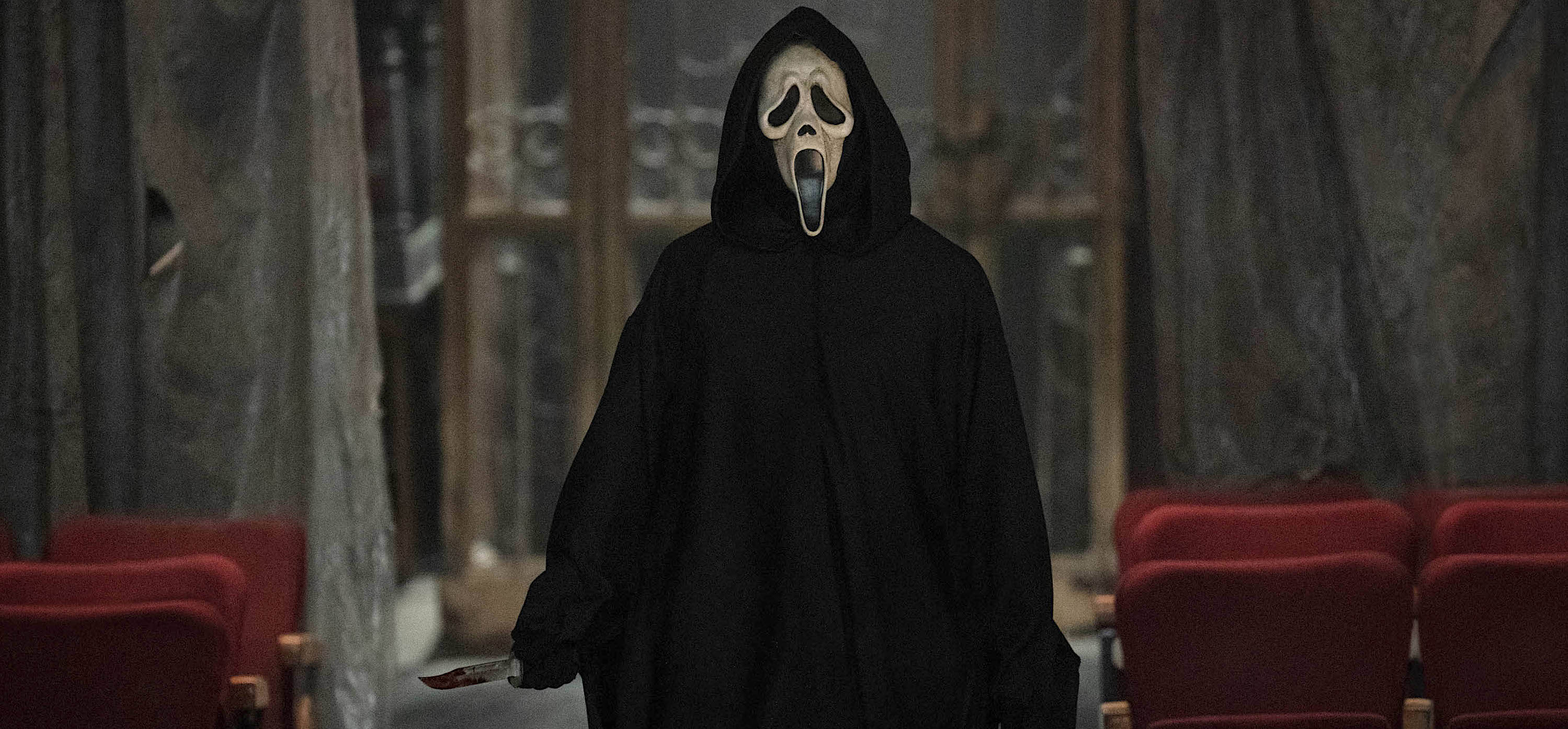 A photo of Scream VI’s Ghostface, with trademark melting scream face and black cloak, holding a knife