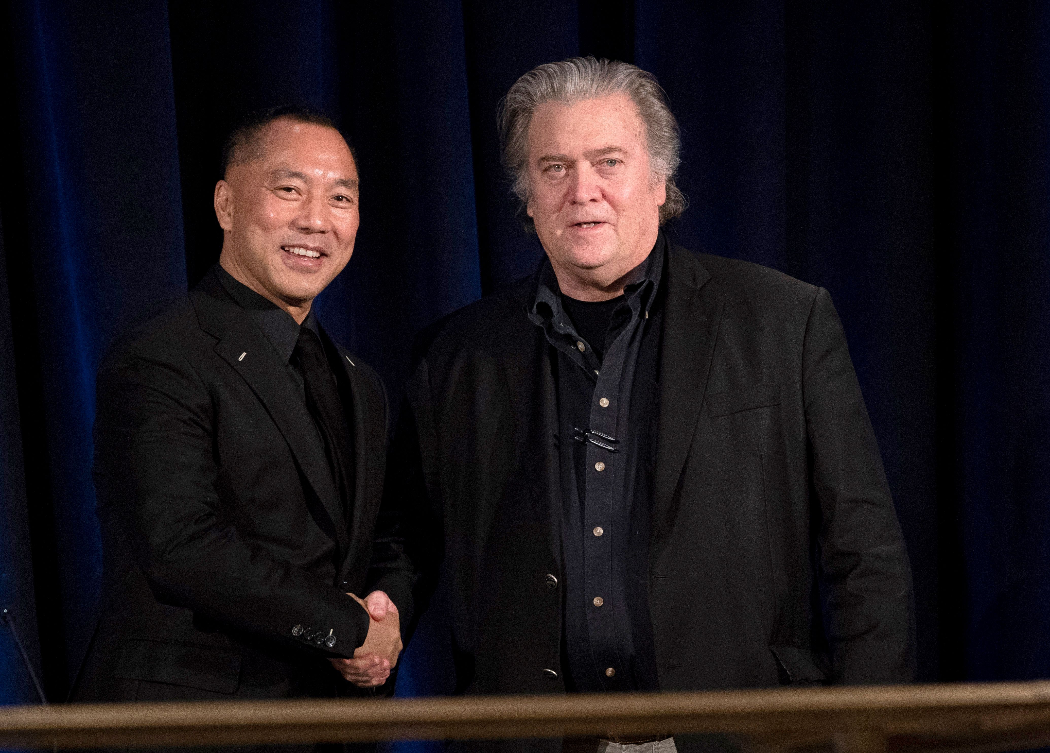Steve Bannon and Guo Wengui shake hands in front of a black background, at the start of a news conference.