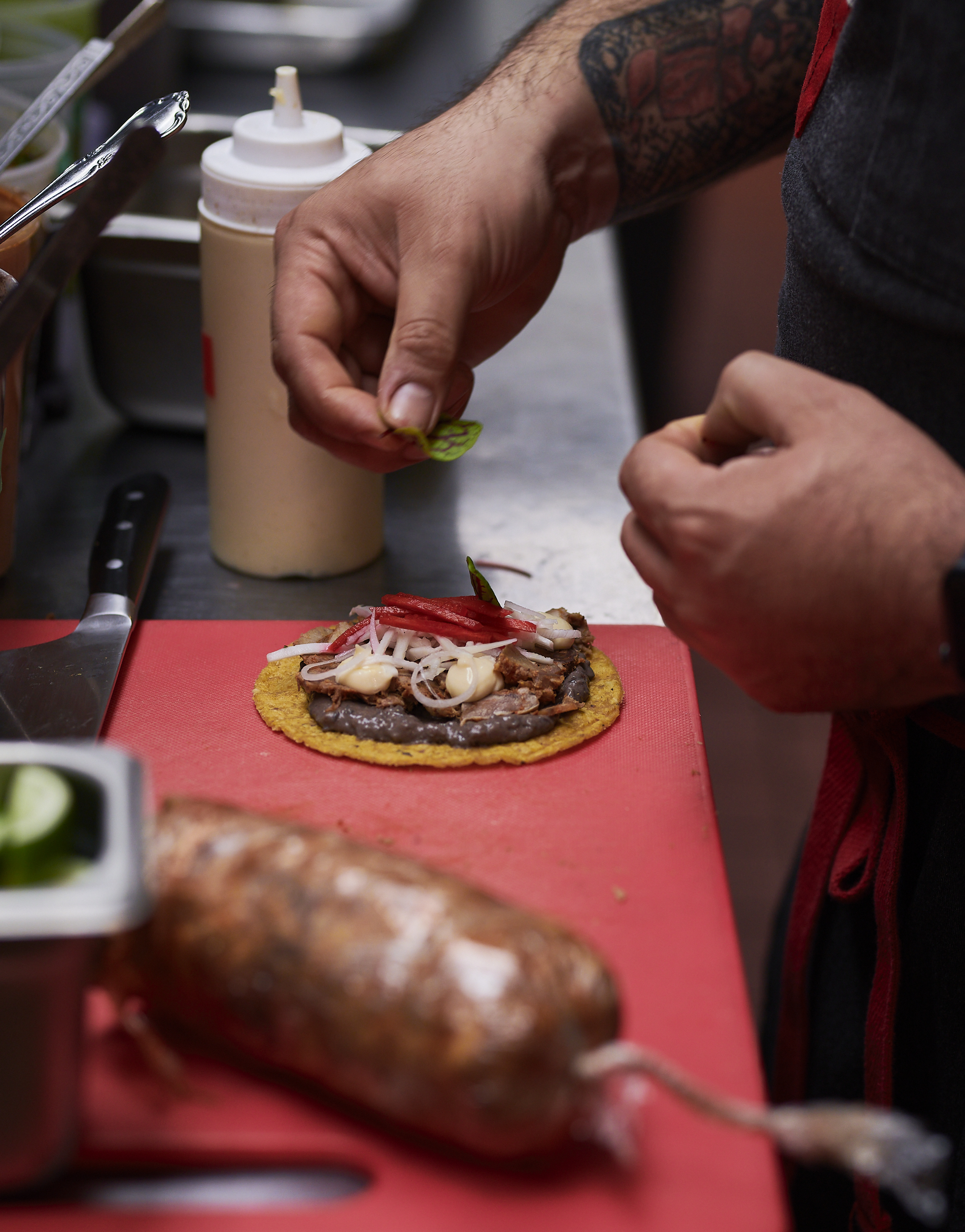 A hand placing an herb on a tortilla topped with beans and veggies on a red cutting board. 