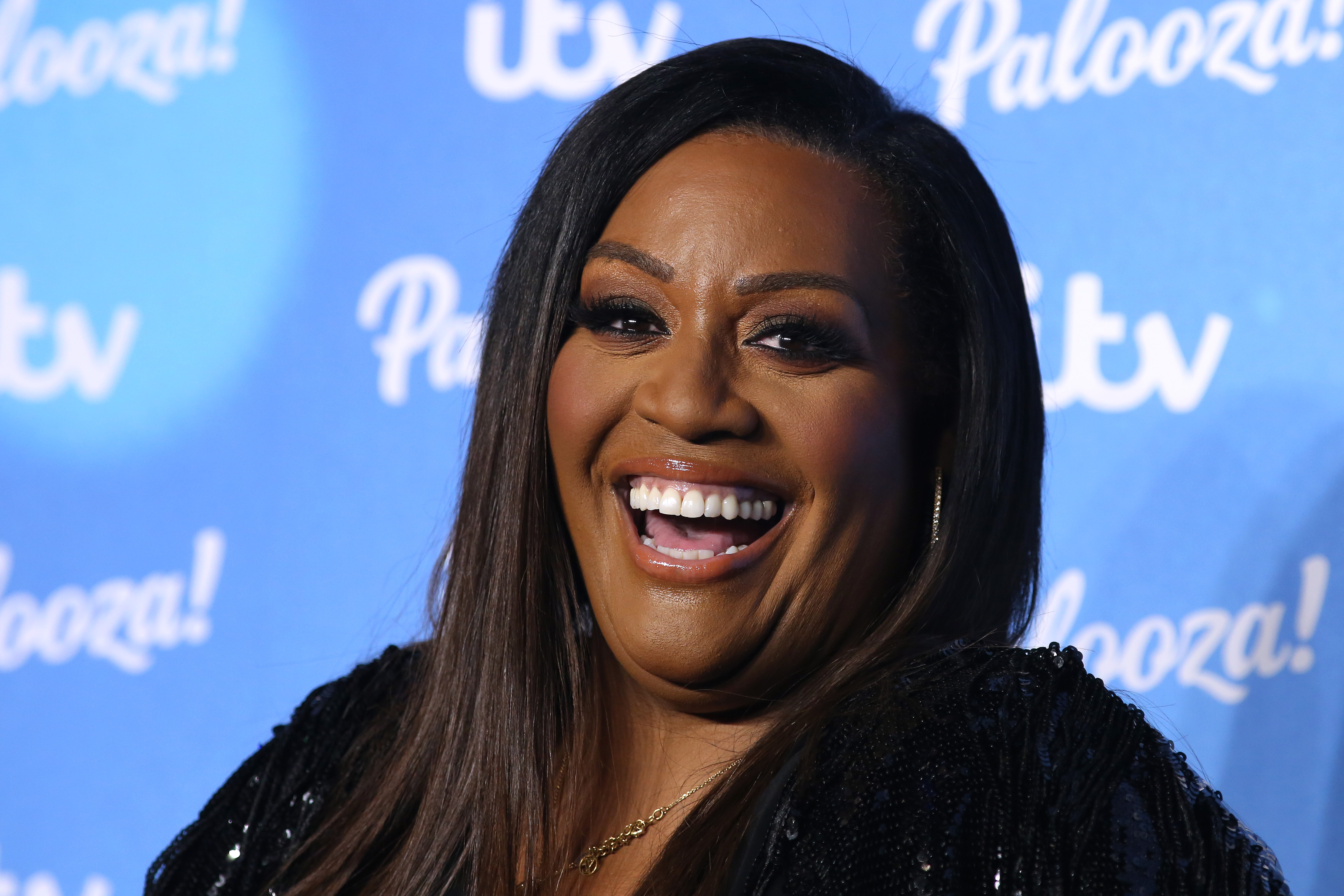 Alison Hammond, a Black woman, smiles in front of a blue backdrop