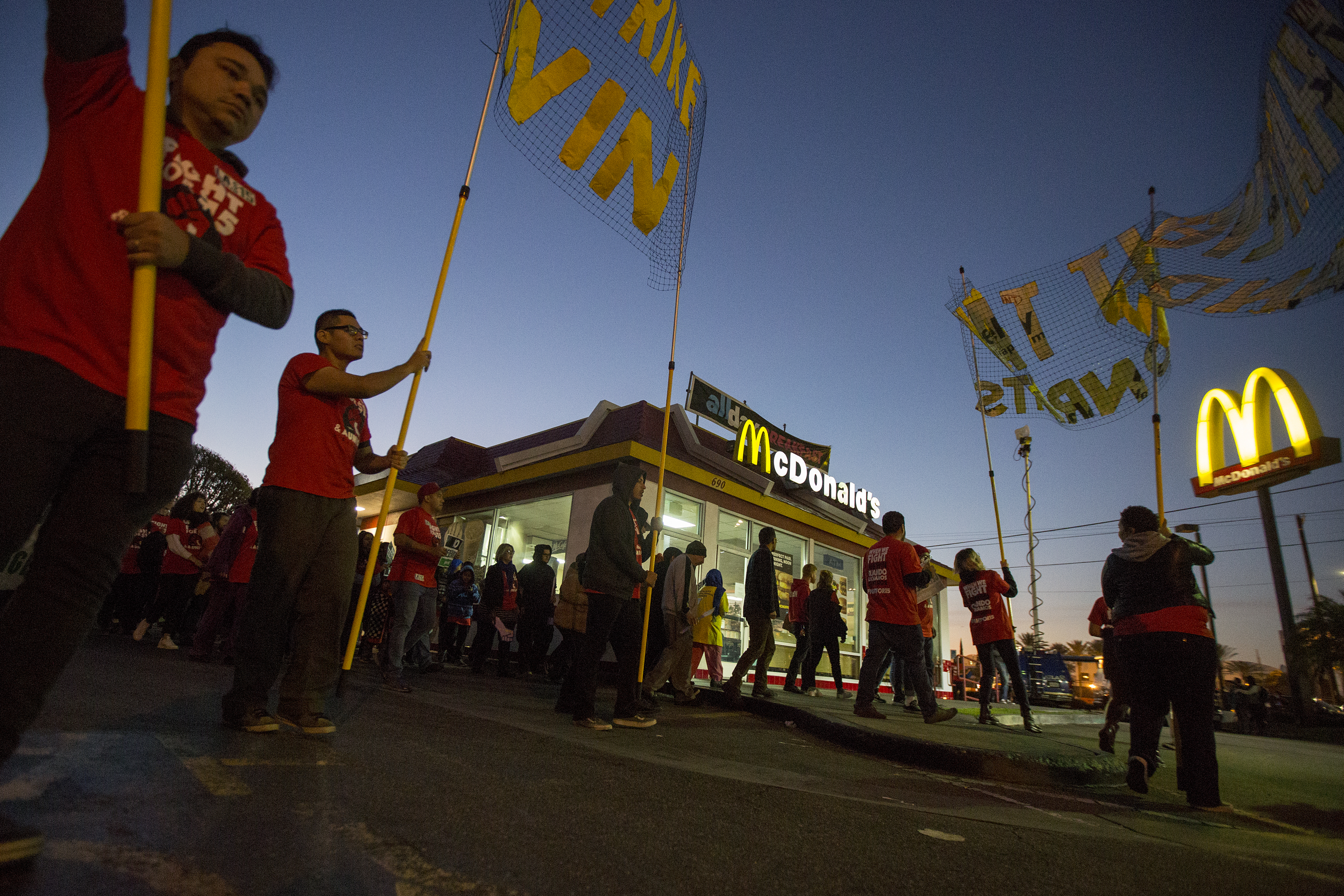 Men holding placards and signs picket outside of a McDonald’s.