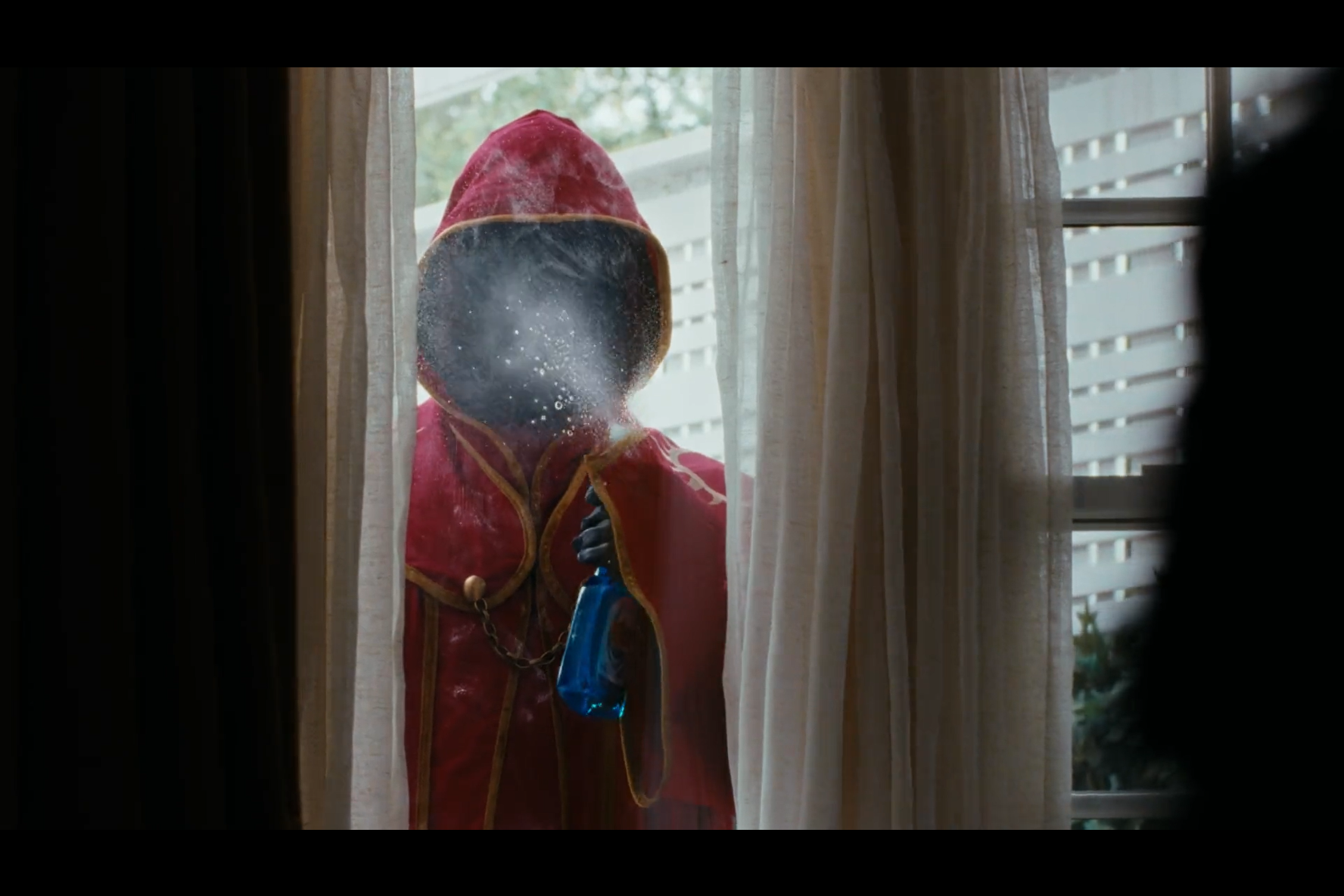 A person wearing a red robe washing a window from outside a house