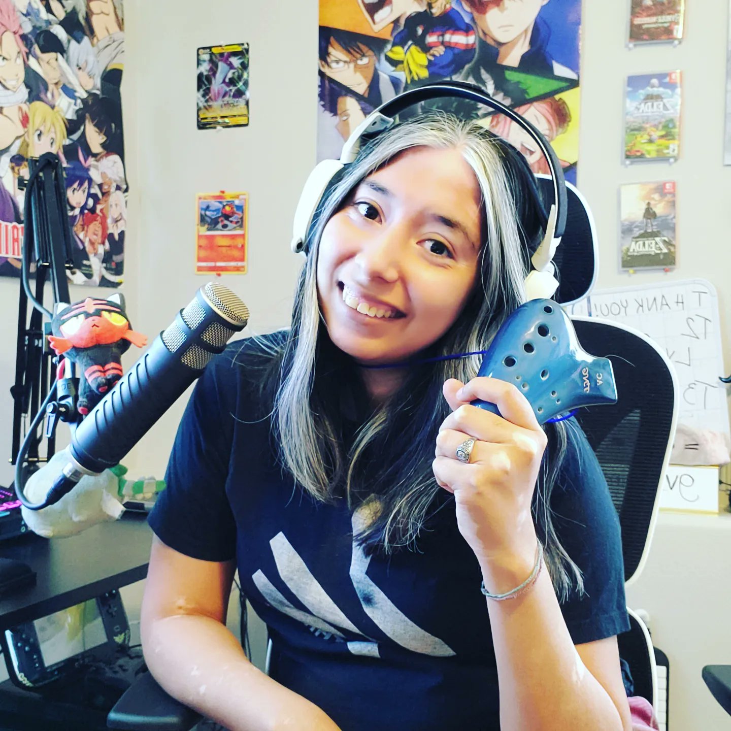 Self portrait of a young woman wearing headphones, holding up an ocarina controller, and leaning into a microphone.