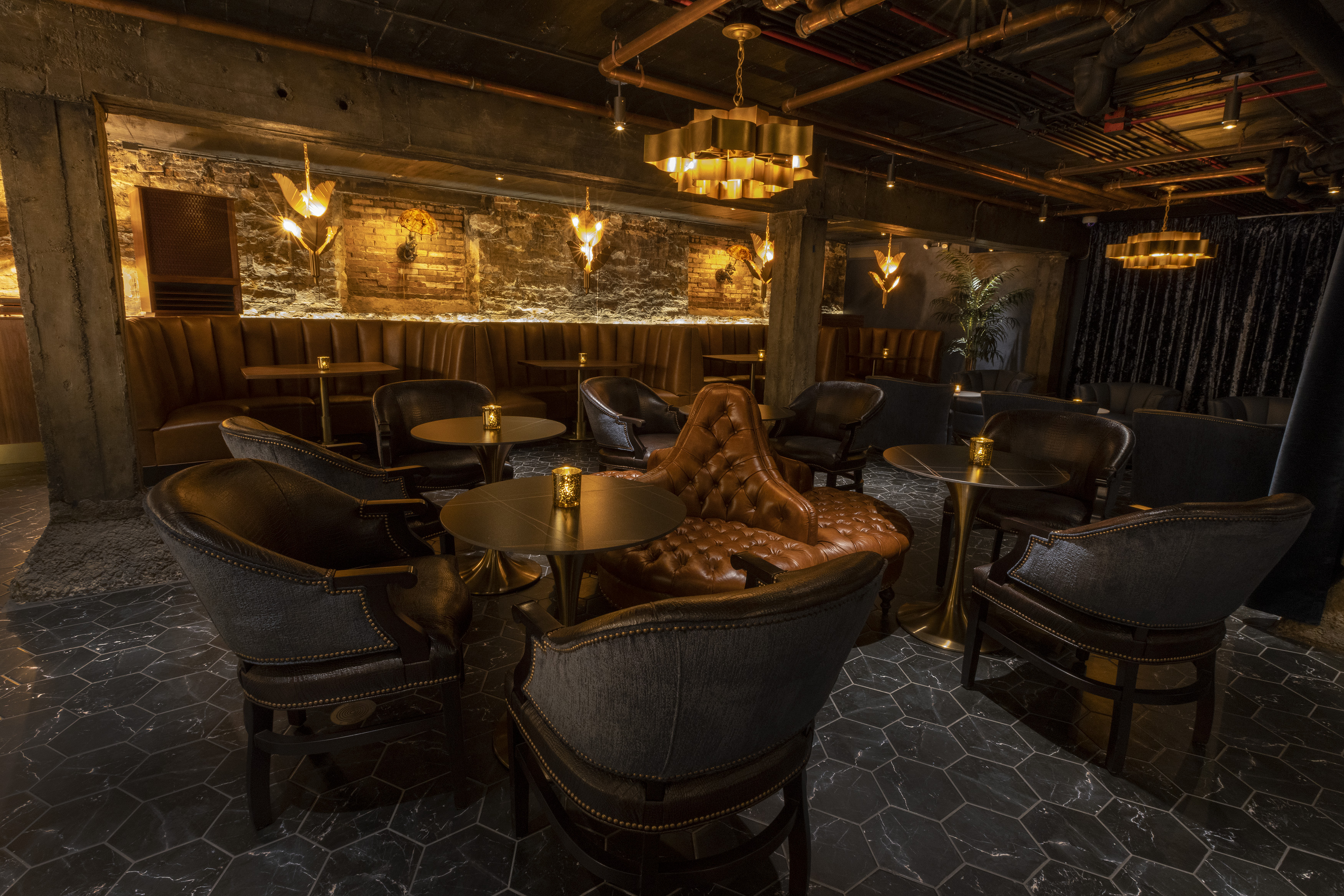 A low-lit speakeasy-style bar filled with leather furniture.