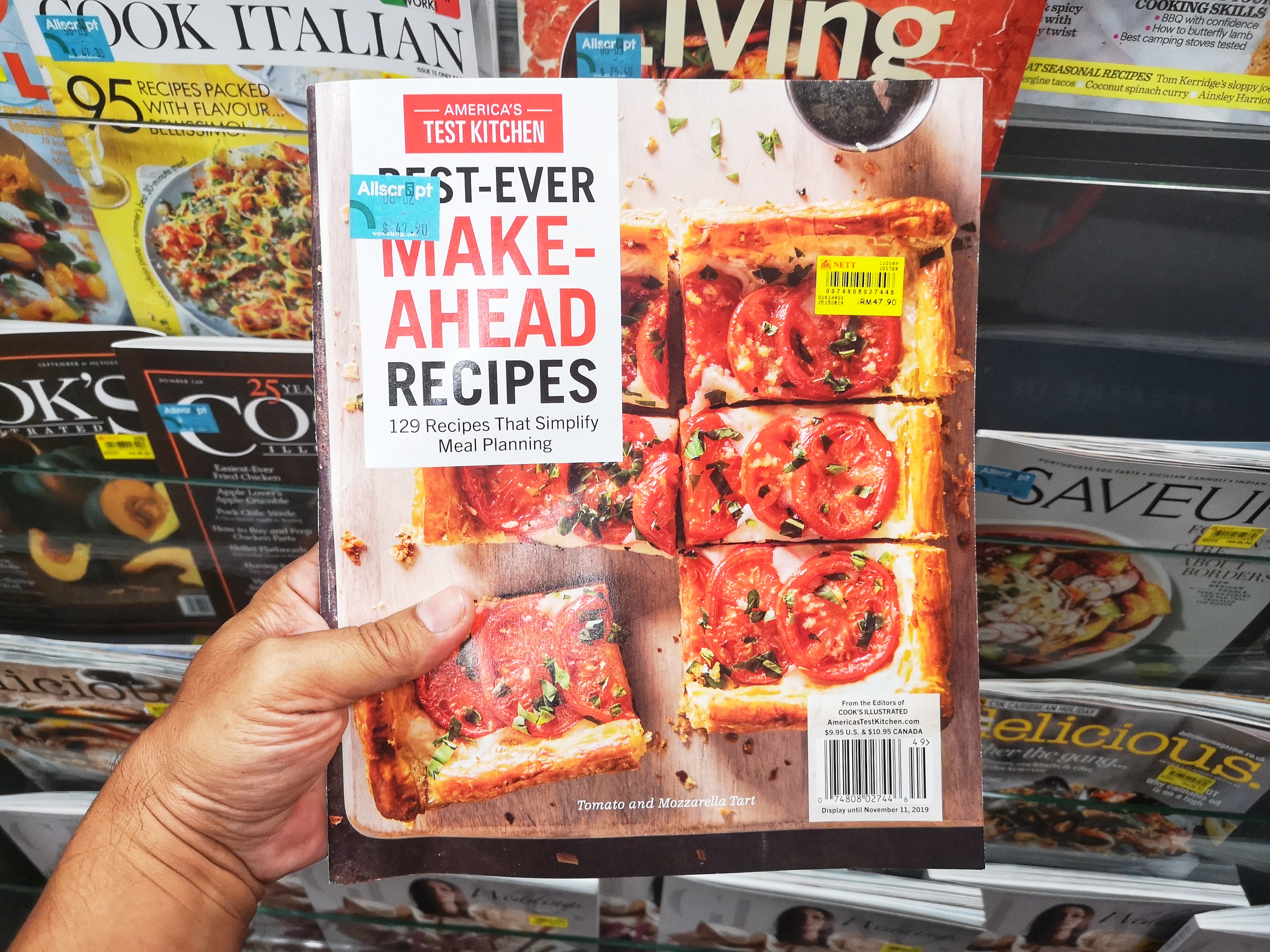 A hand holds up a copy of the America’s Test Kitchen magazine with a sliced pizza on the front cover.