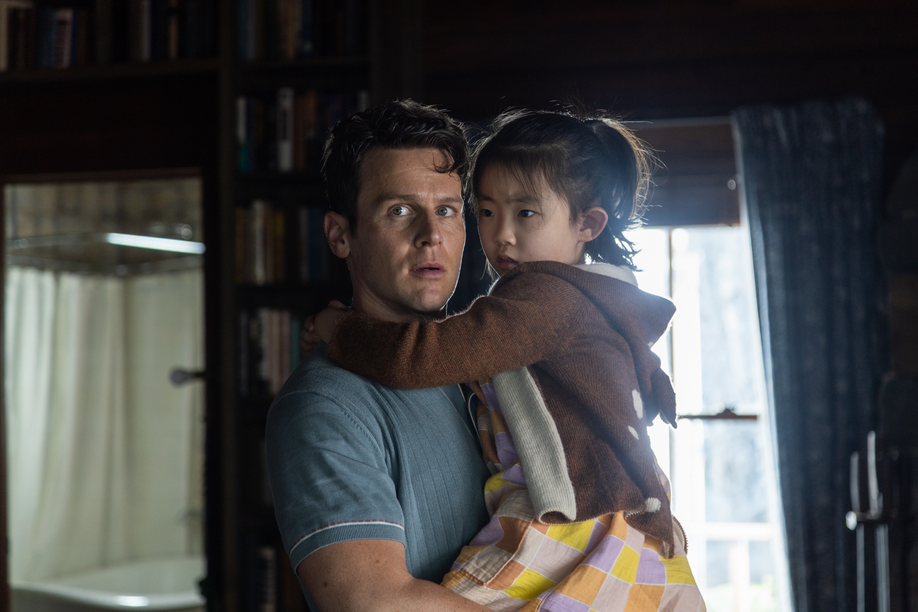 Eric (Jonathan Groff) holds a young girl Wen (Kristen Cui) in his arms in Knock at the Cabin