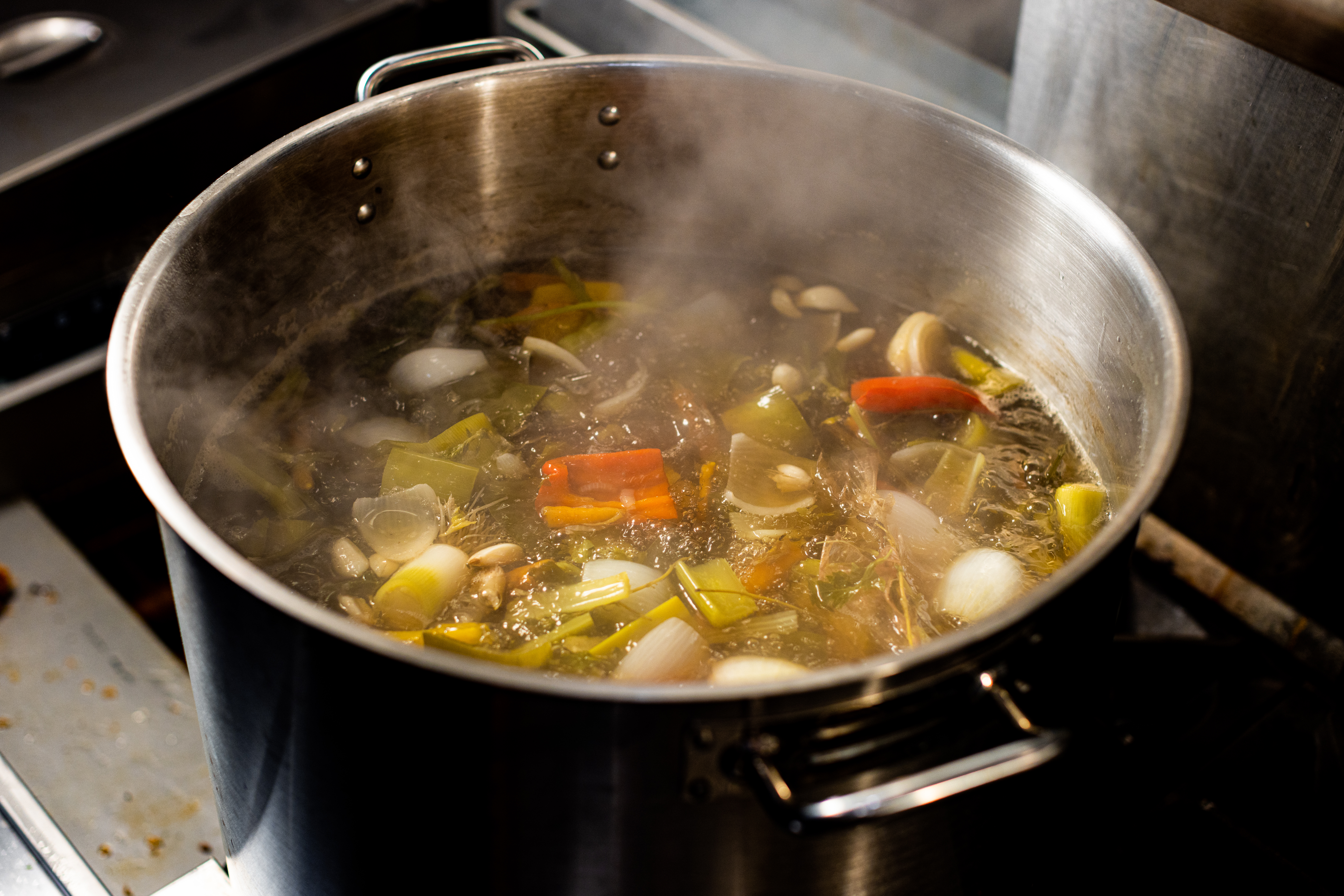 A boiling pot holds carrots, onions, and bell peppers.