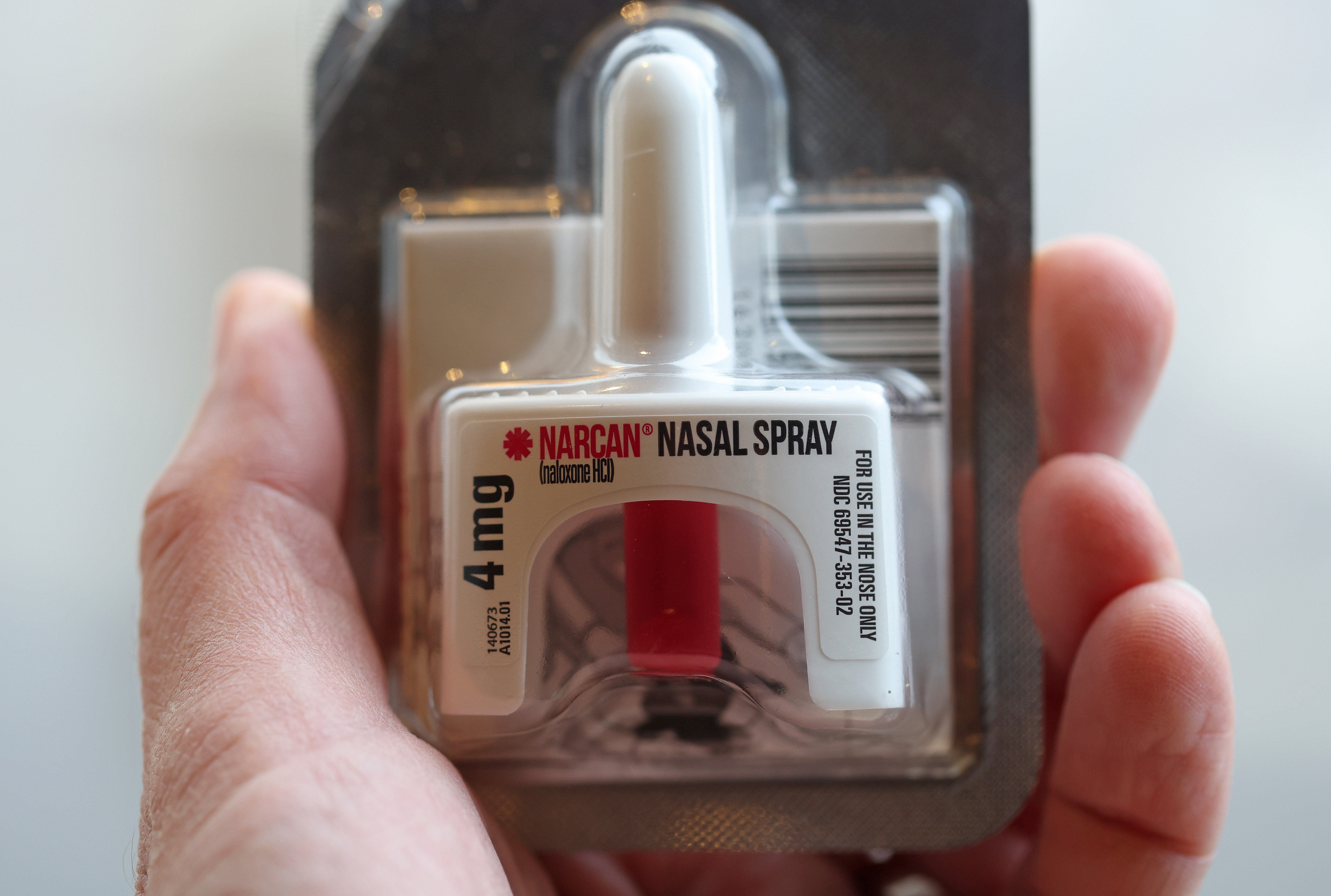 A photo of a hand holding the small cartridge of Narcan nasal spray.