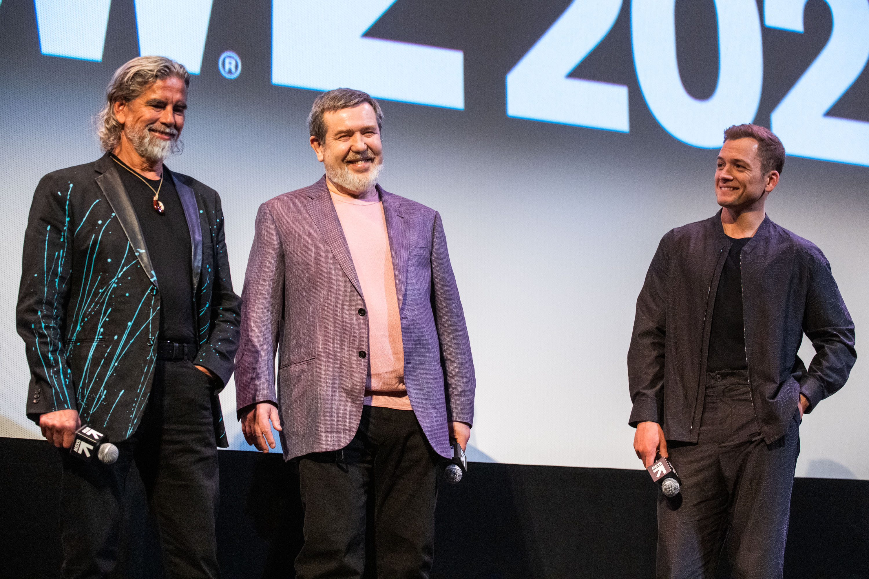 Henk Rogers, tanned with long silver hair, and Alexey Pajitnov, with a white beard, stand next to each other smiling and wearing flashy jackets over plain T-shirts.