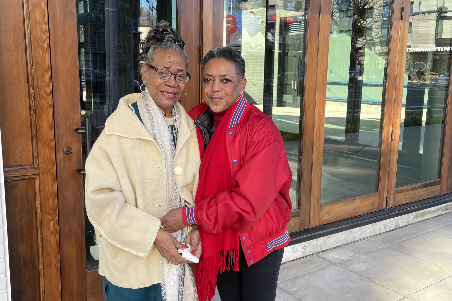 Two Black women stand in front of a storefront