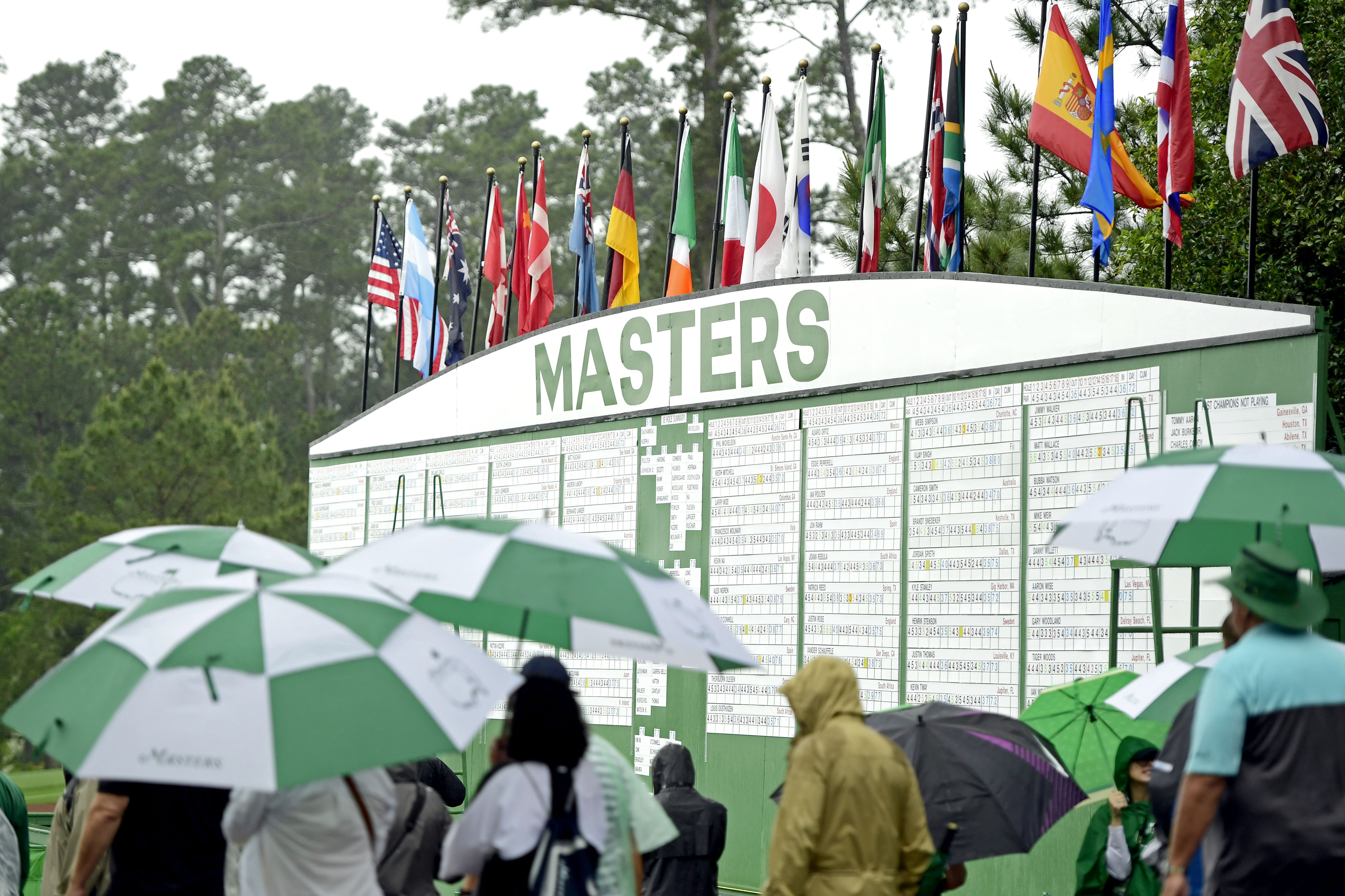 Patrons walk by the the leader board as rain falls during the second round of the Masters at Augusta National Golf Club, Friday, April 12, 2019.