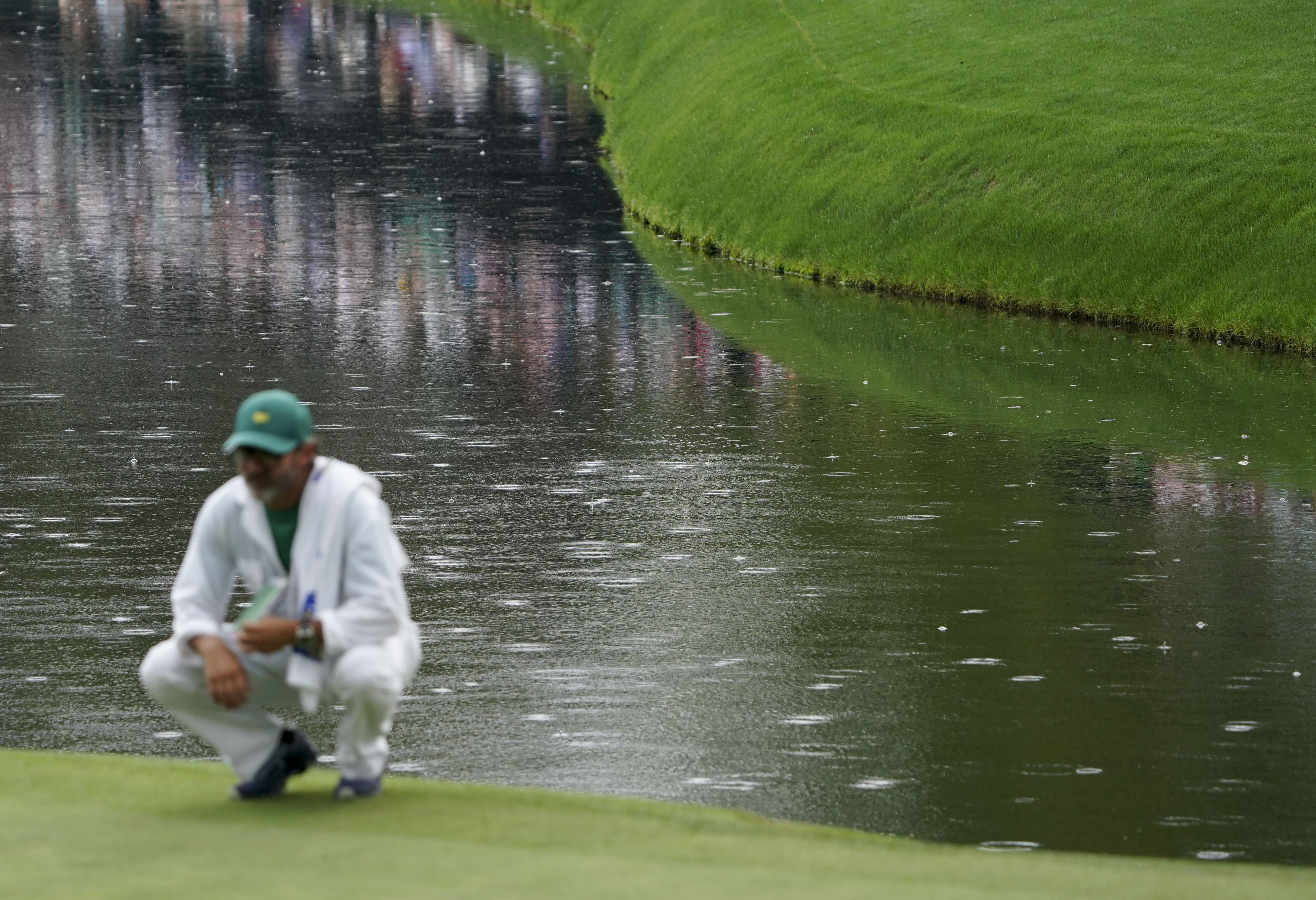 Corey Conners caddie surveys the no. 16 green as rain hits the pond behind him during the second round of The Masters golf tournament.