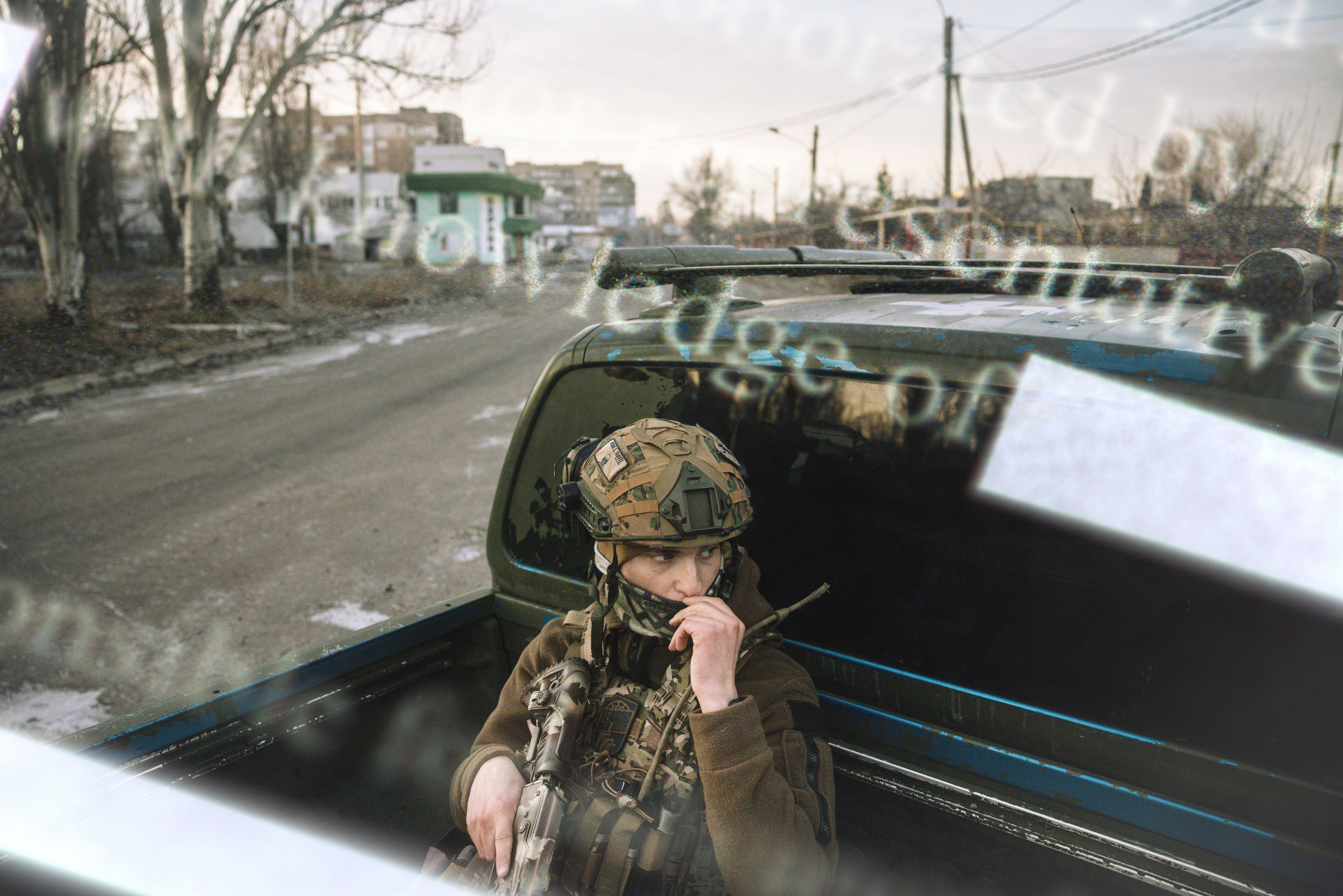 A photo illustration of a Ukrainian soldier patrolling the streets of Donetsk, sitting in the back of a black pickup truck. Superimposed on the photo are words representing recently leaked documents, like “knowledge of.” 