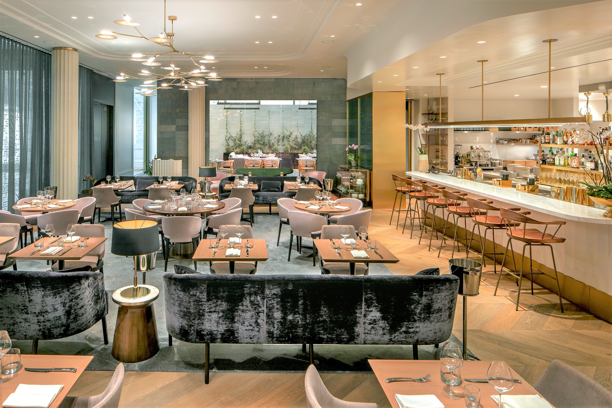 An upscale French restaurant dining room at daytime with plush seats and an open kitchen.