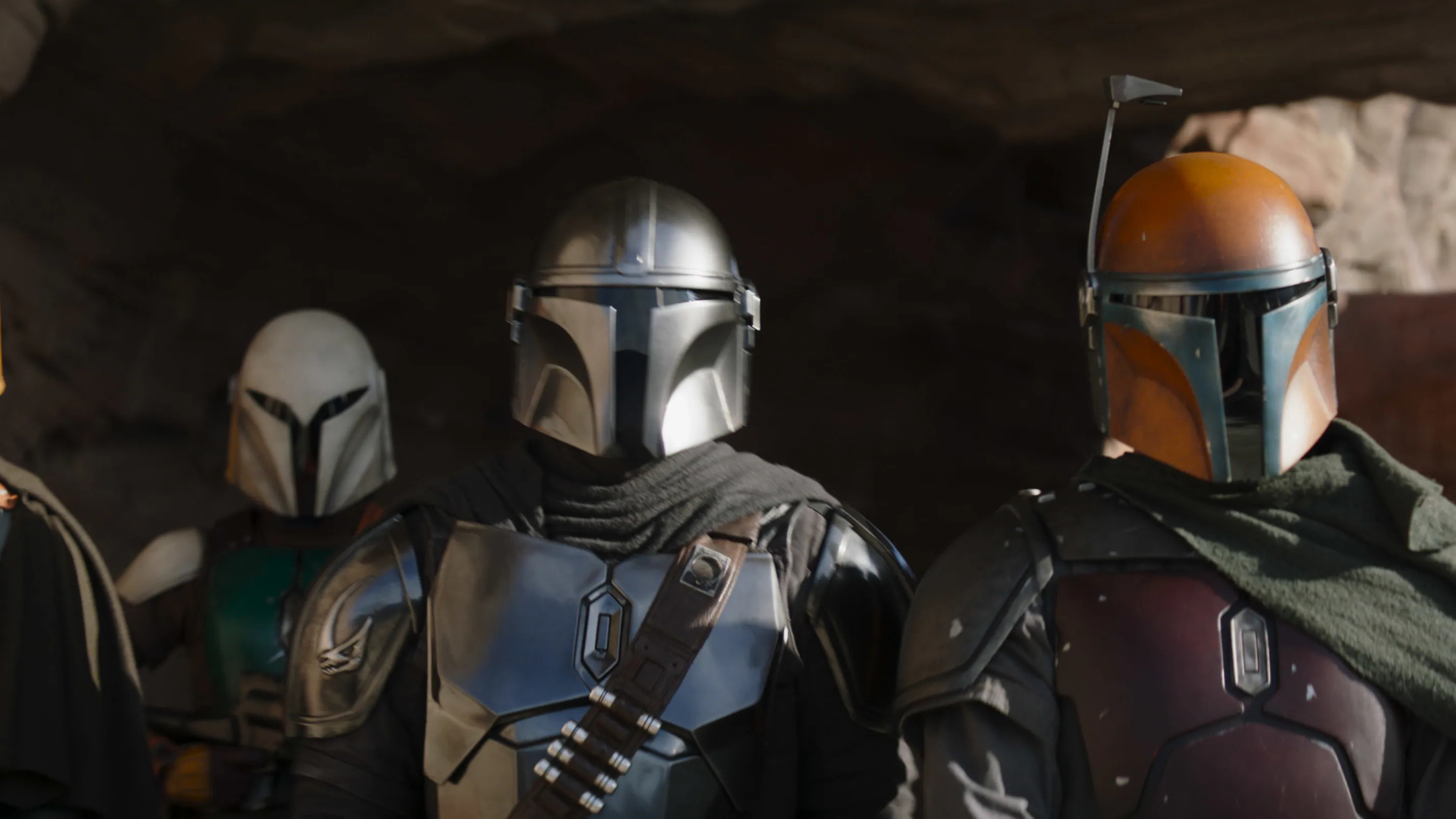 A shot from the TV show The Mandalorian shows three Mandalorian fighters in their distinctive helmets and armor, with a variety of weapons.