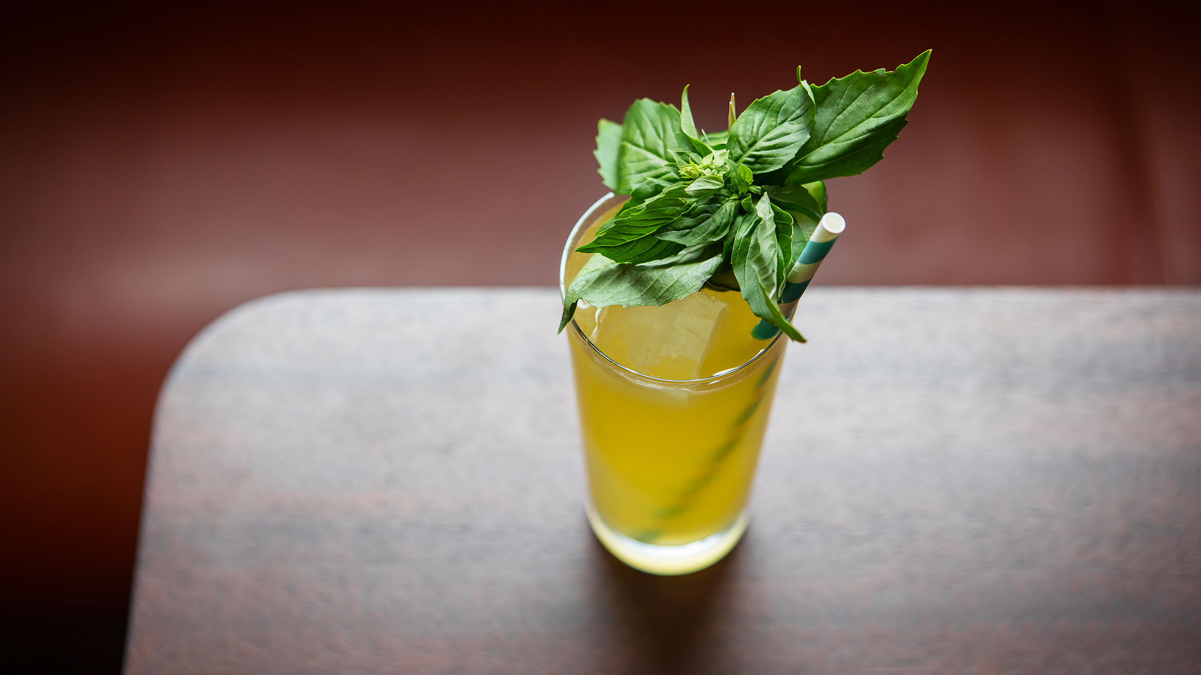 A yellow beverage in a tall glass with mint garnich and paper straw.