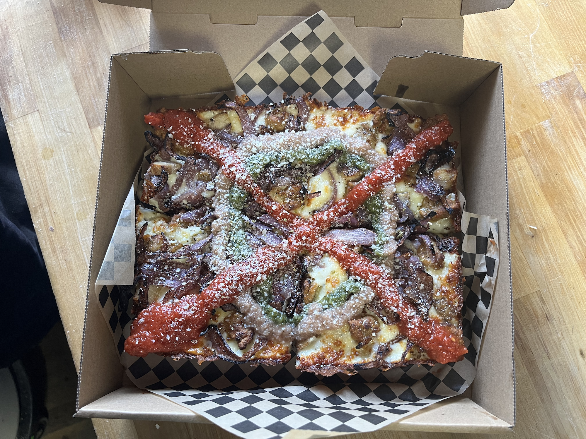 A Detroit-style pizza topped with several colorful sauces