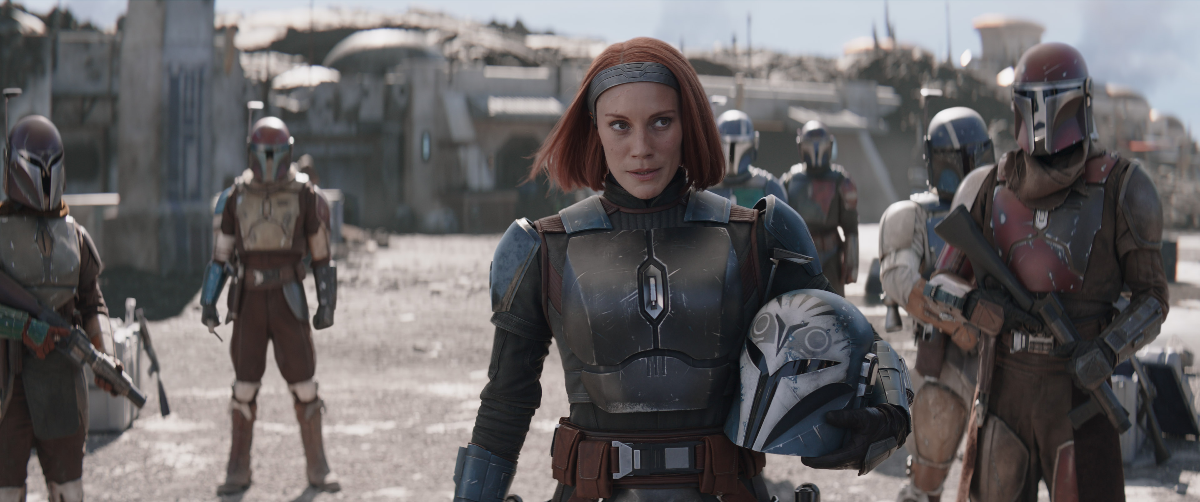 Bo-Katan stands with her helmet off amidst her fellow Mandalorians in season 3 of The Mandalorian.