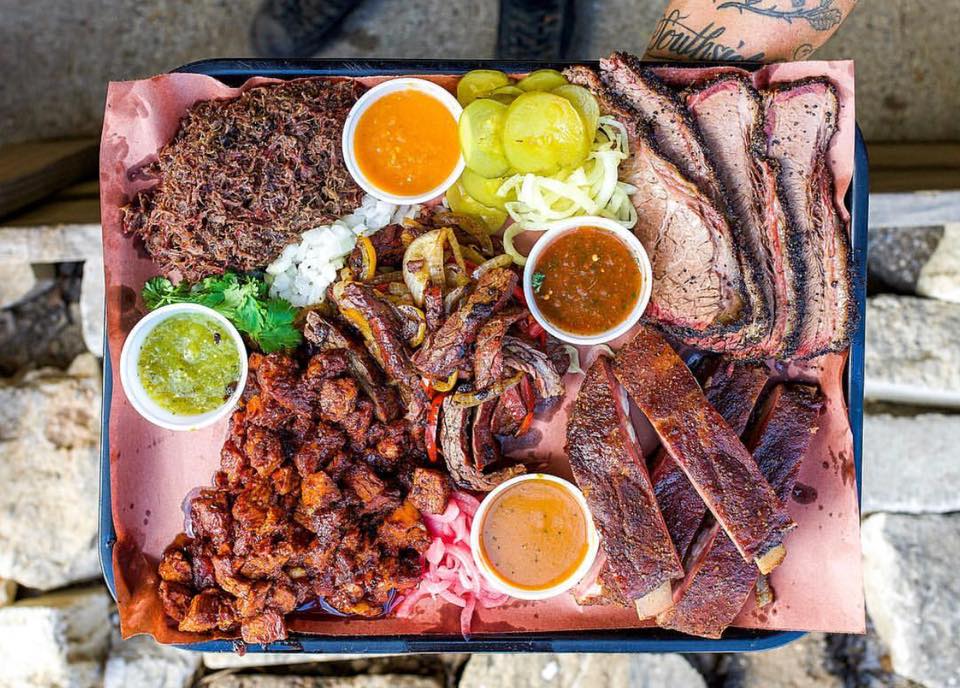 A tray of barbcued meats and sauces and sides.