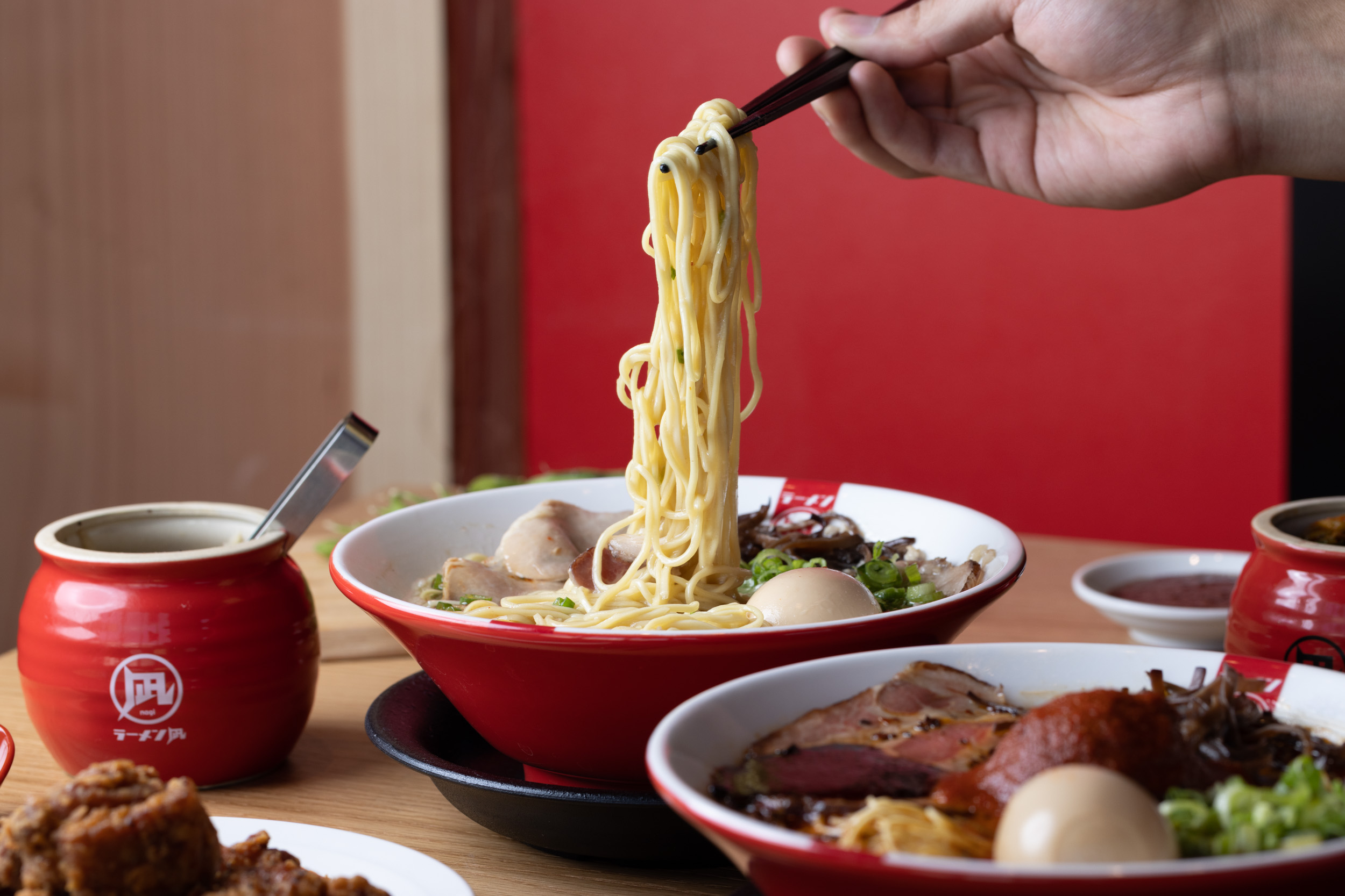 A hand holding chopsticks lifts noodles from a bowl of ramen.