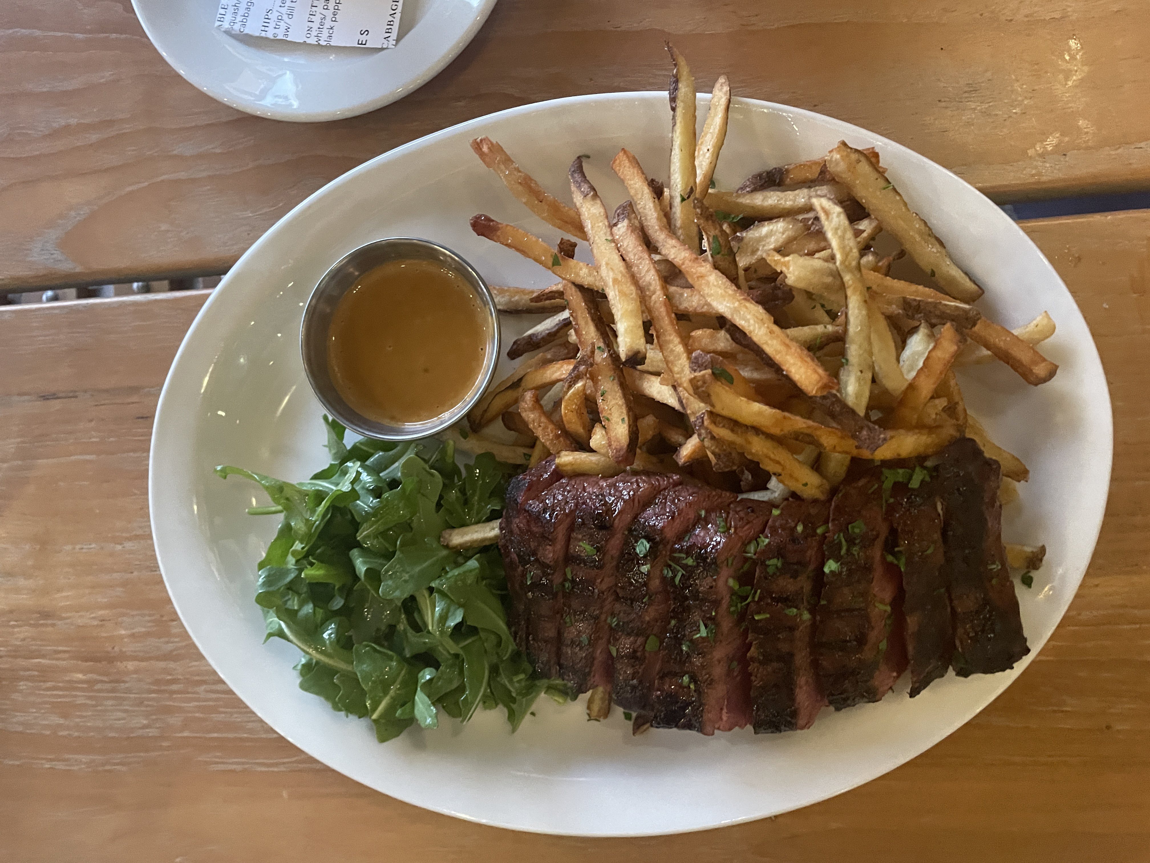 A white plate holds a sliced steak, french fries, an arugula salad, and dressing.