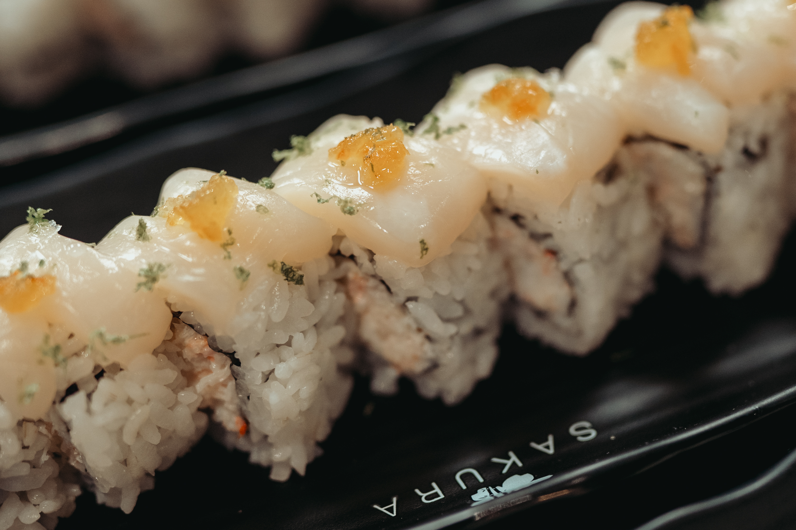 A close-up of a sushi roll topped with scallop and marmalade.