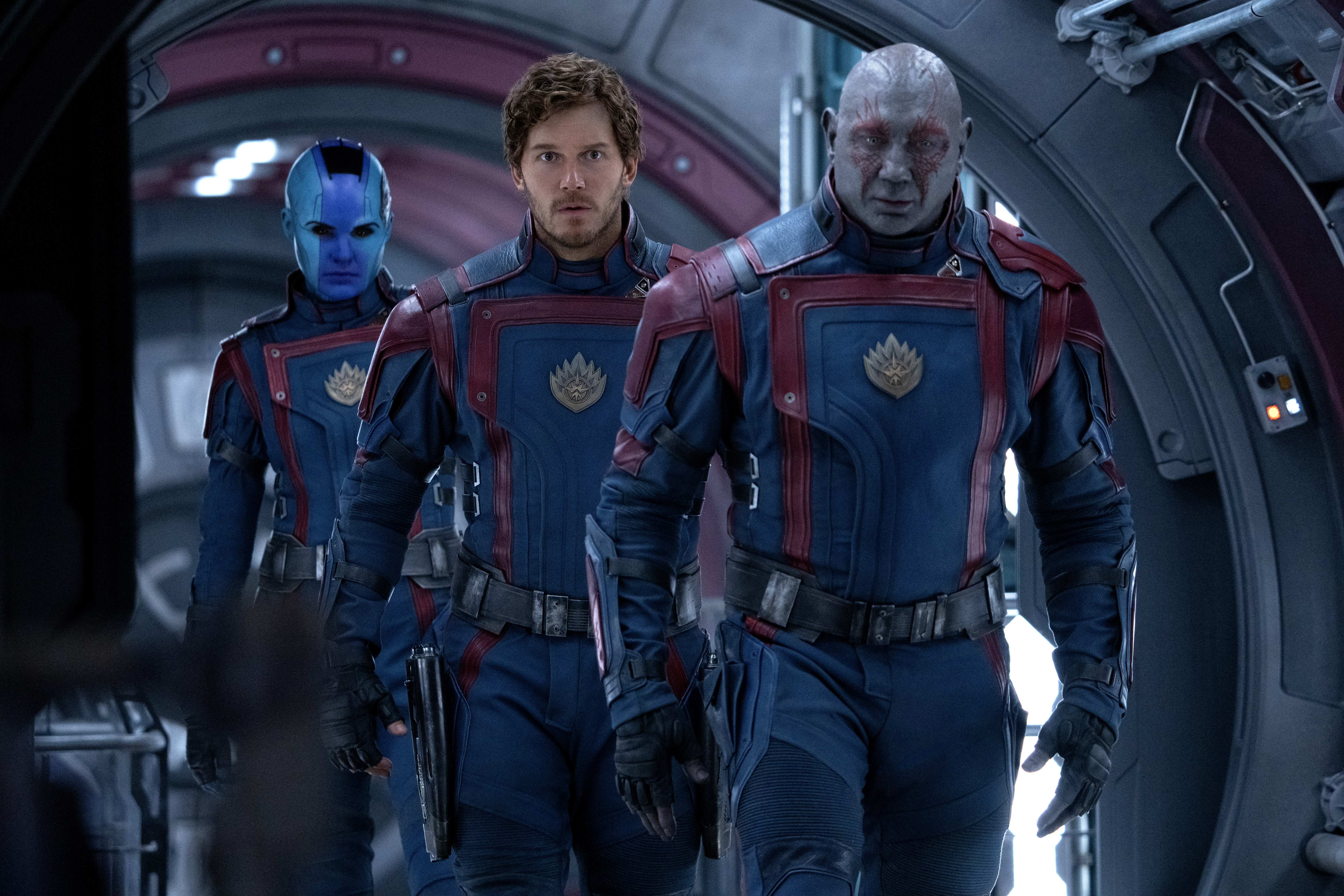 Star-Lord (Chris Pratt), Drax the Destroyer (Dave Bautista), and Nebula (Karen Gillan) walk through a ship hallway in uniform in Guardians of the Galaxy Vol. 3