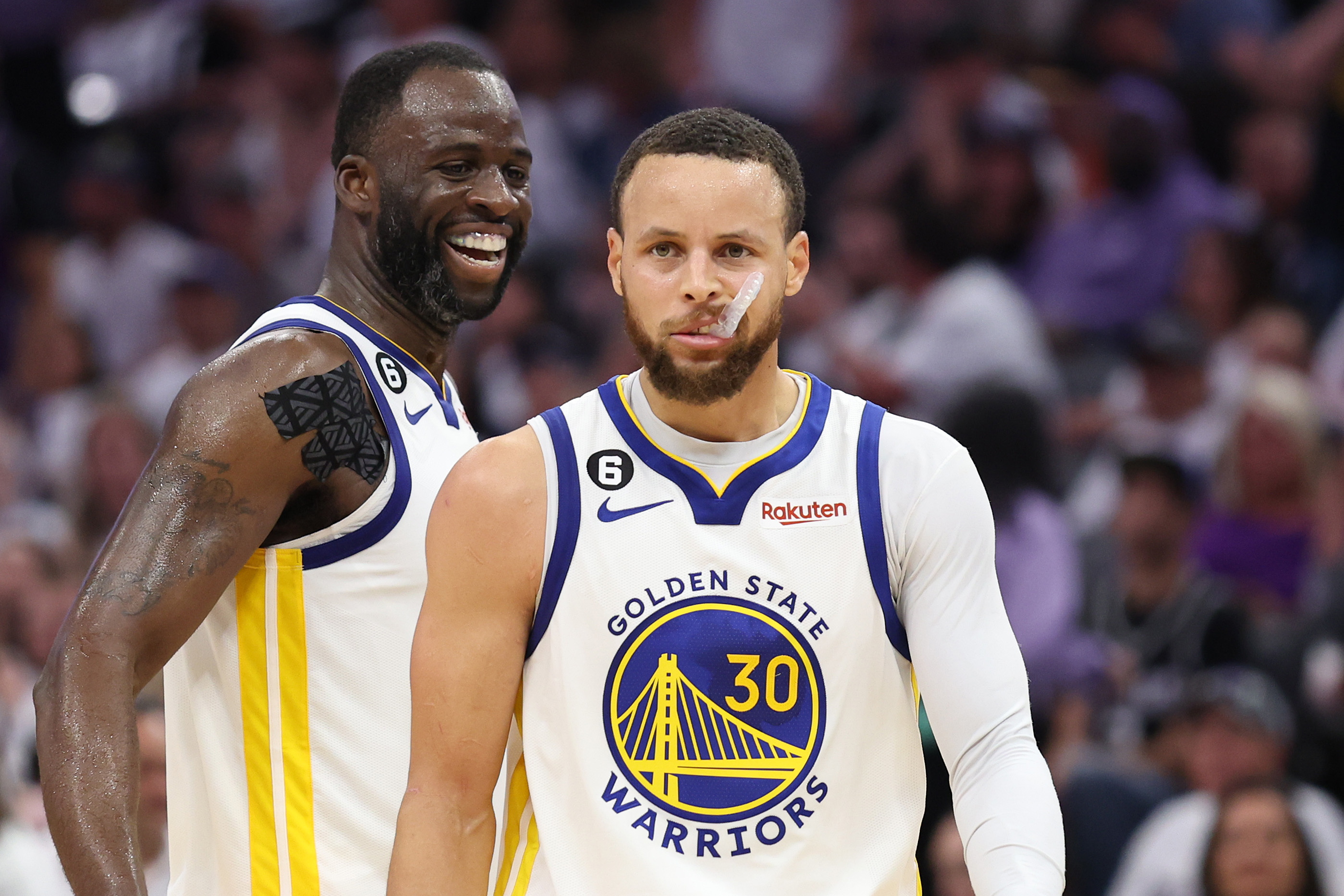 Steph Curry looking determined while Draymond Green smiles behind him