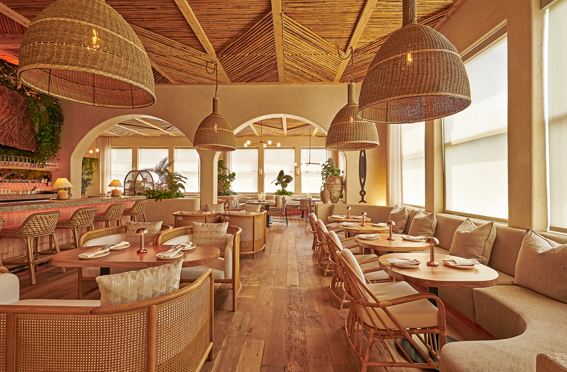 A golden dining room with wooden floors, curved banquettes, and wicker covered hanging lamps.