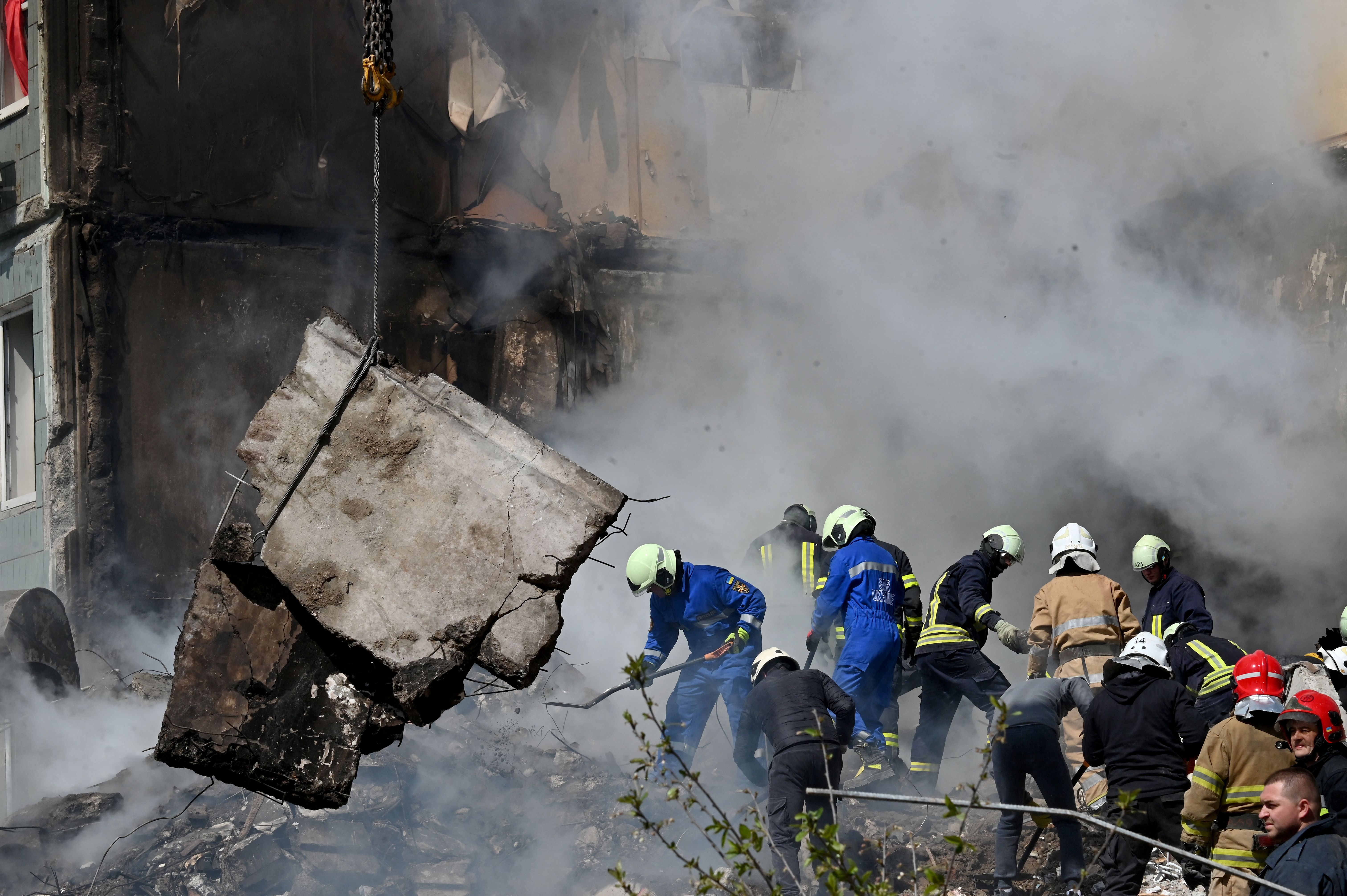 Rescue workers in helmets surrounded by rubble with smoke in the air. 