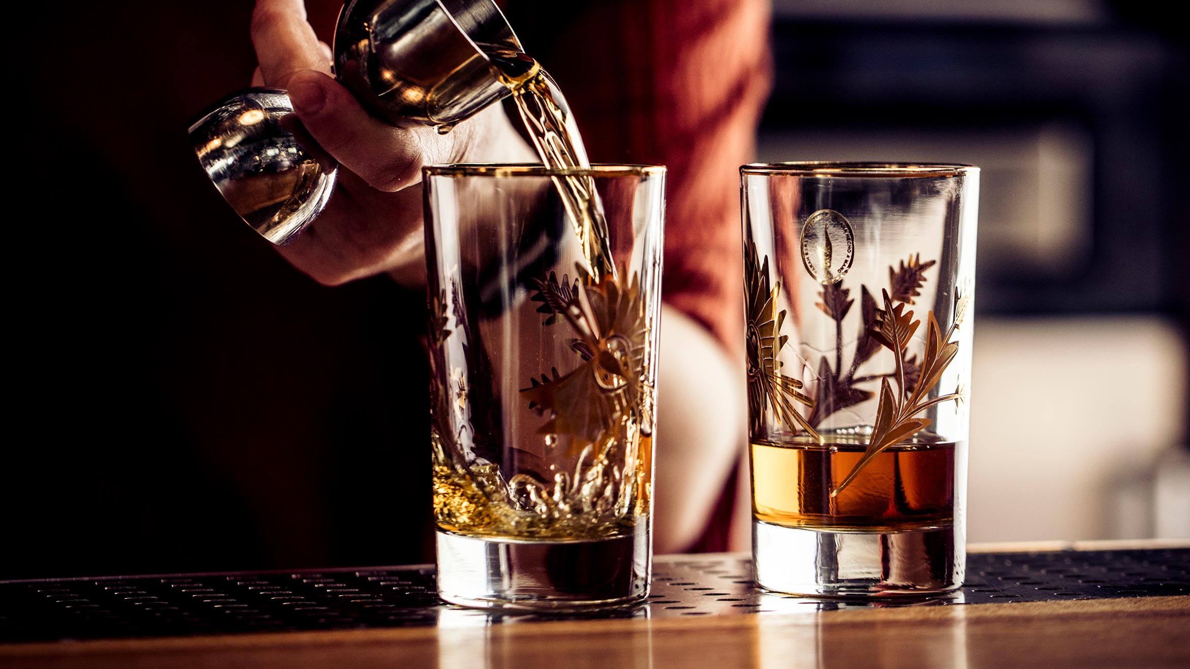A bartender pours a shot from a jigger into a shot glass 