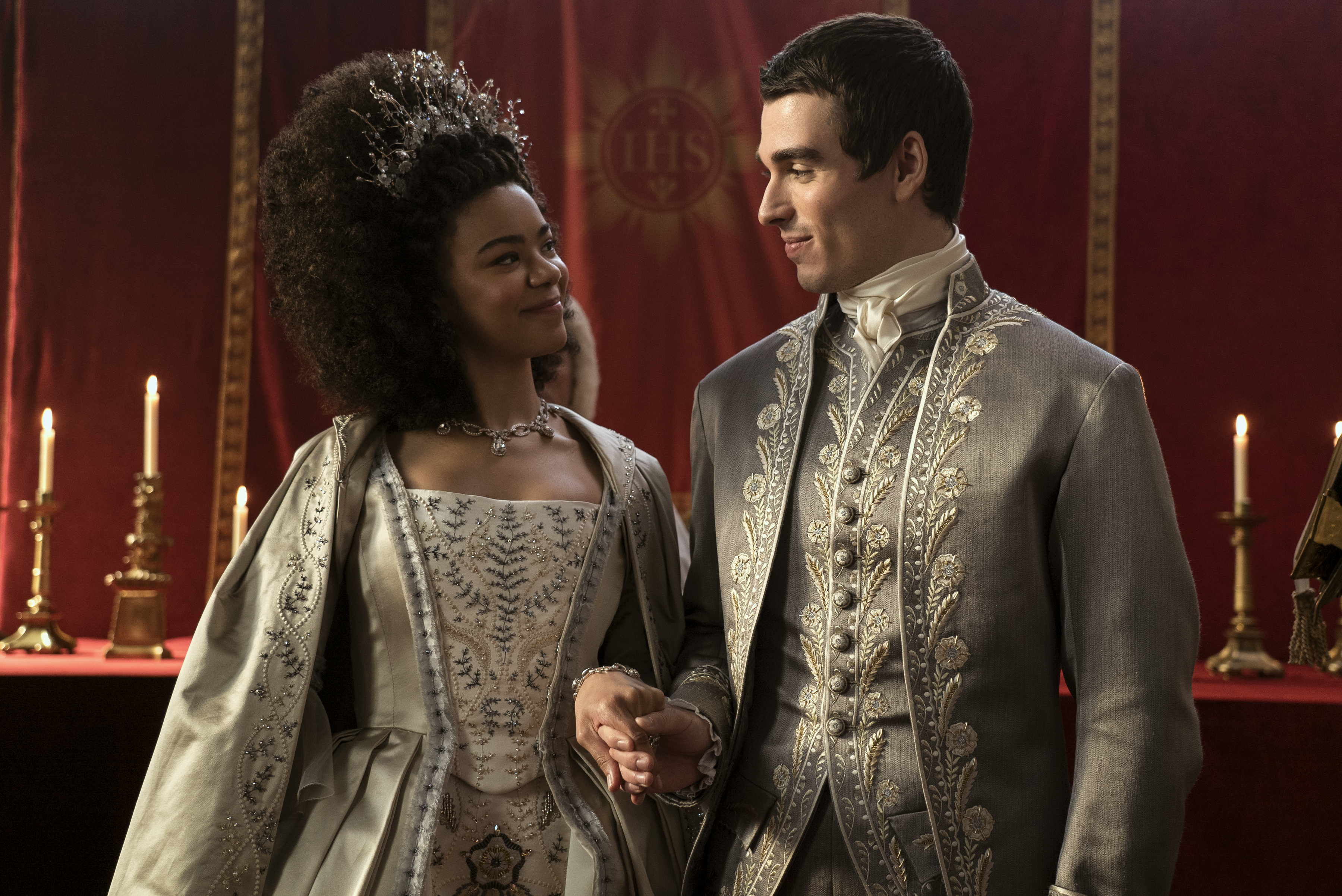 A young Black queen in Regency dress, looking next to her at her young white king.