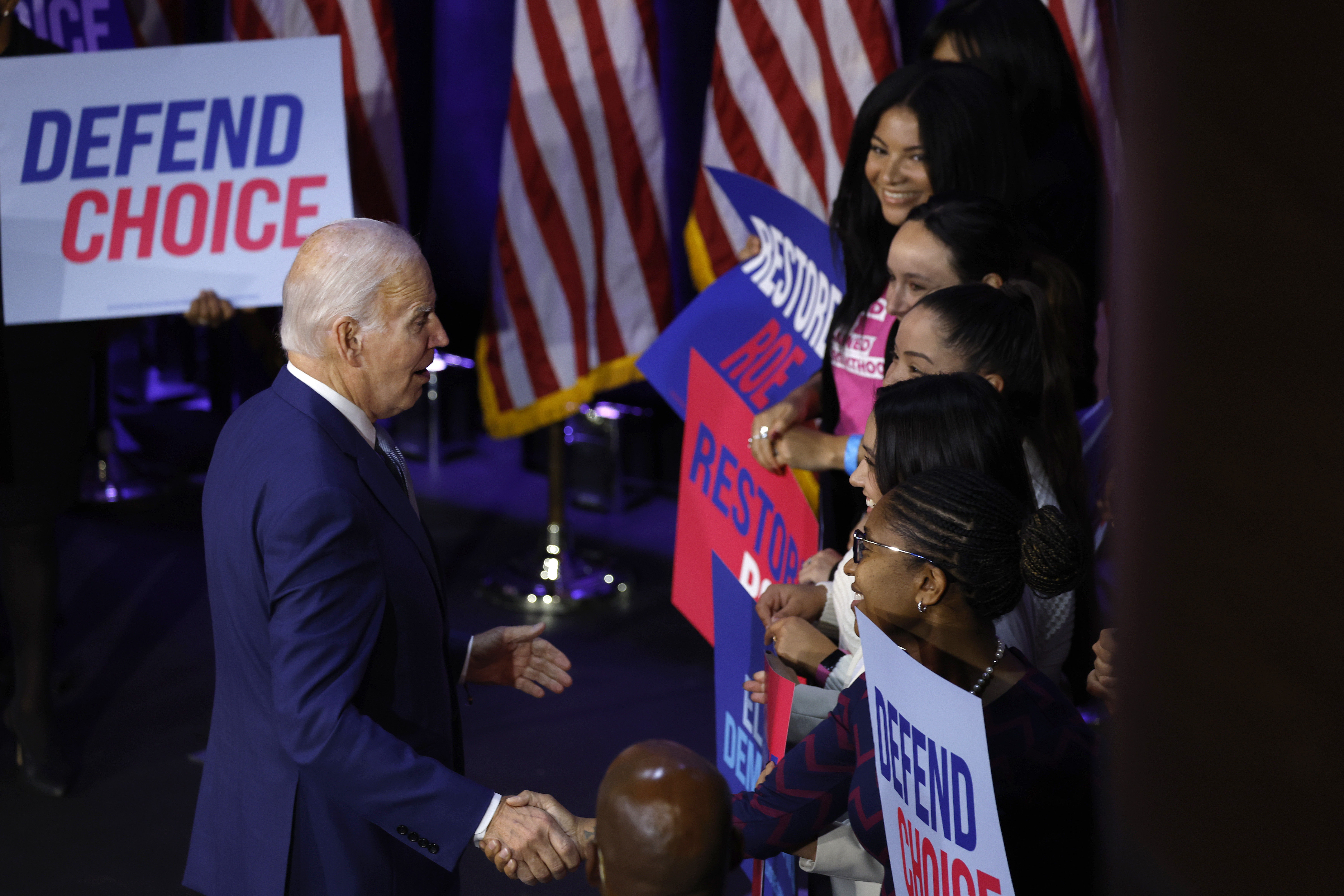 Joe Biden seen from the side shaking hands with a line of supporters holding signs that say Defend Choice.