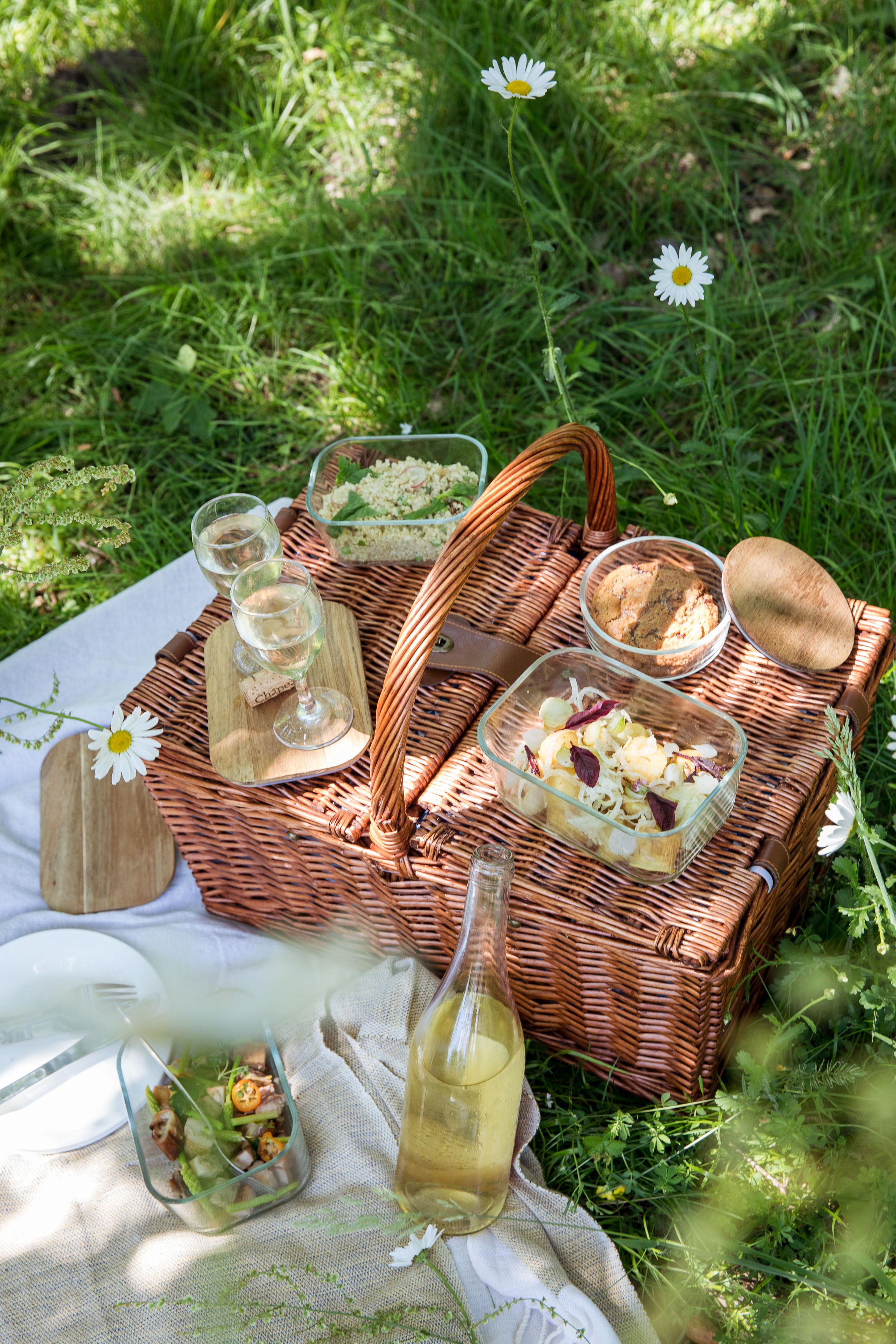 A picnic basket with various dishes and wine in a flowery field.