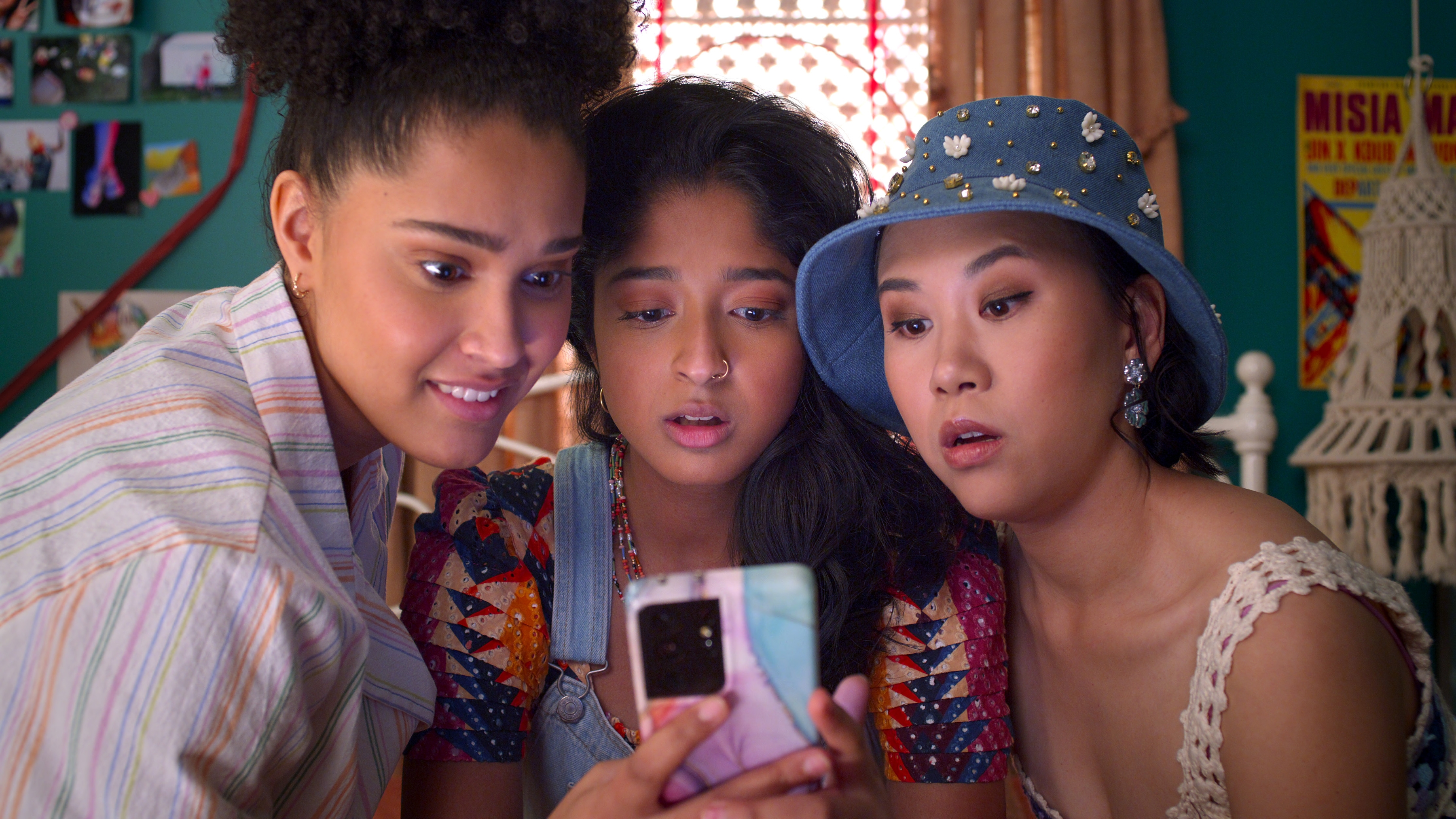 Fabiola, Devi, and Eleanor eagerly gather around Devi’s phone to read something.