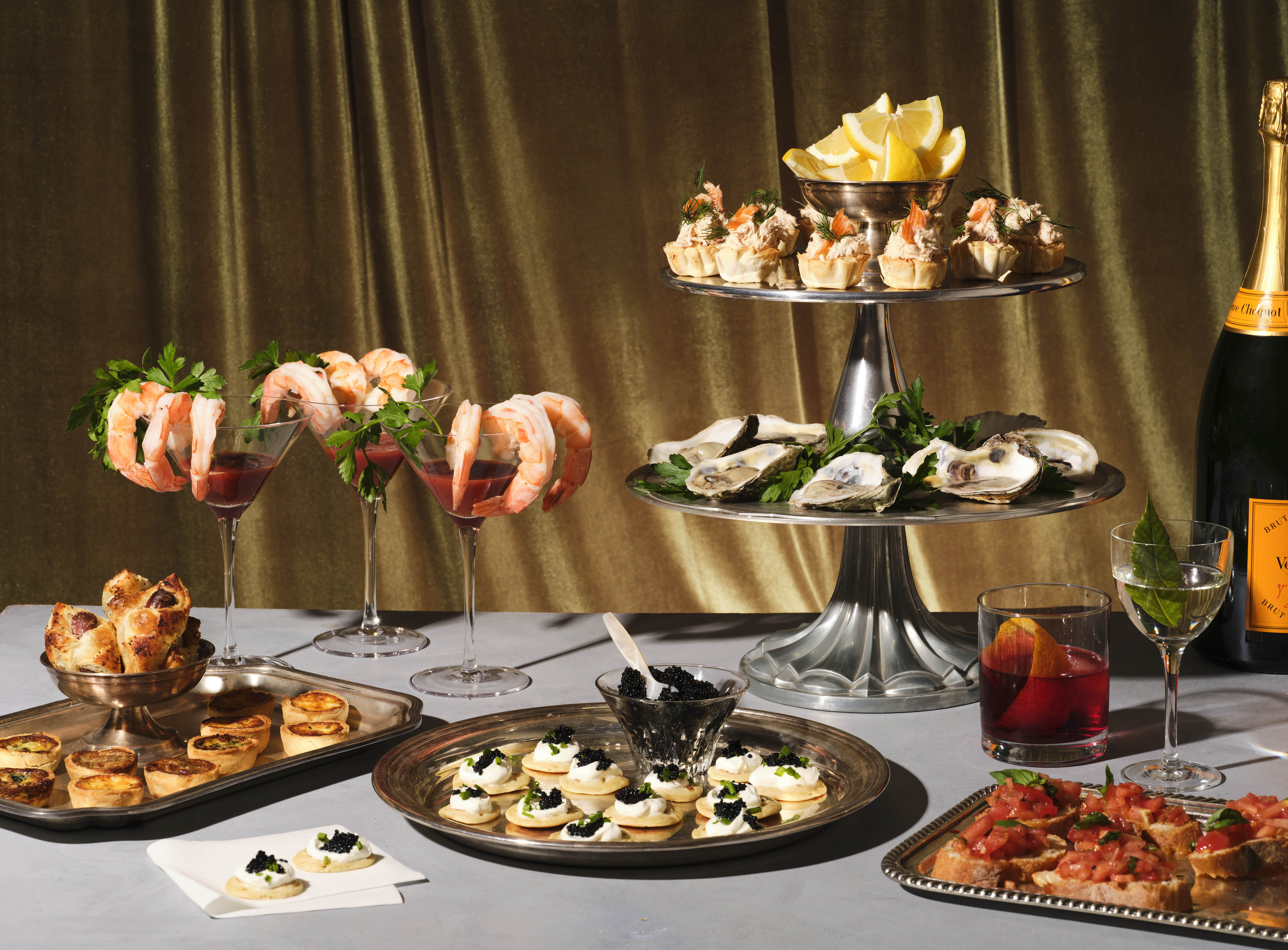 A table set with an array of appetizers, including shrimp cocktail, oysters, blinis, and canapes.