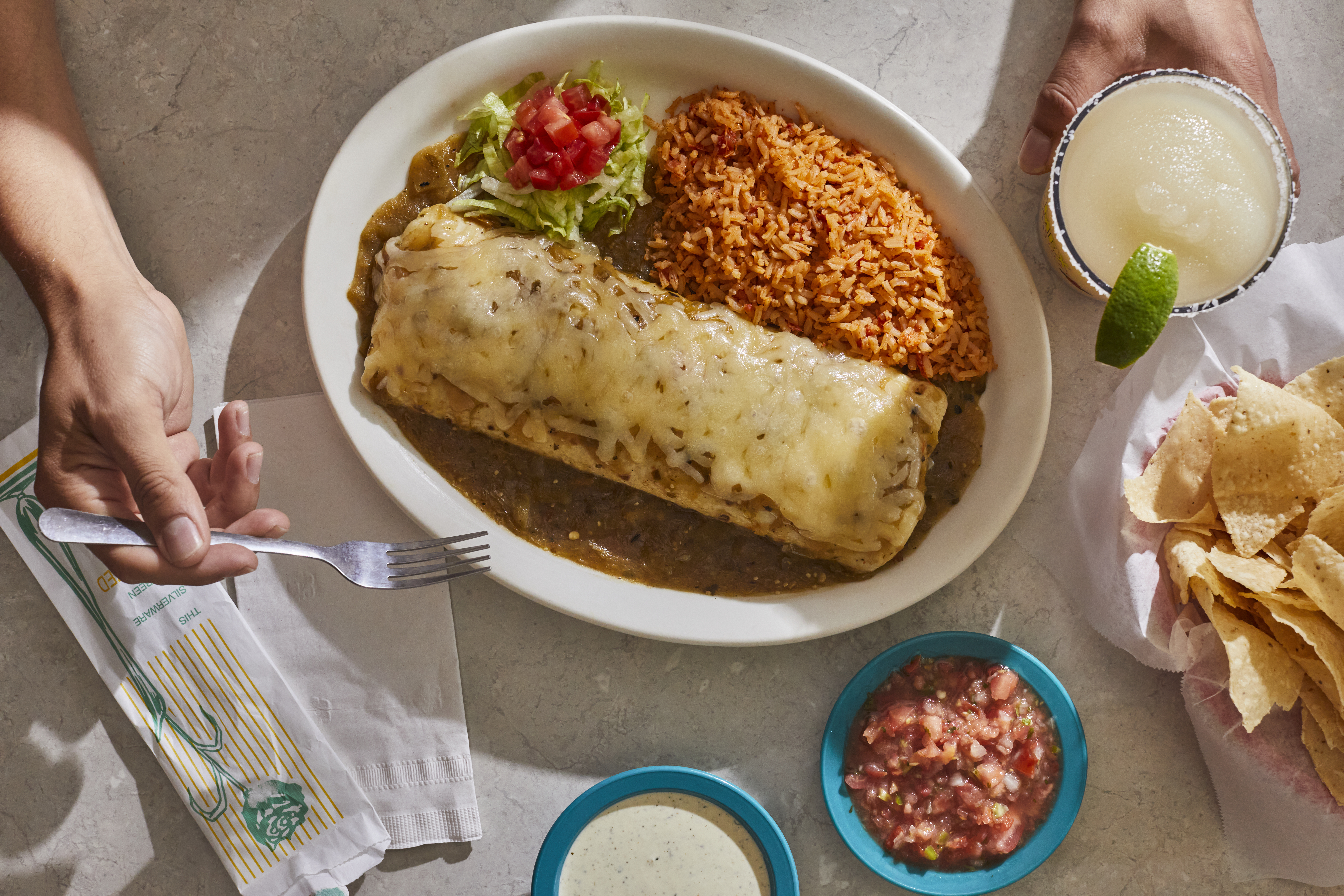 A plate of a burrito smothered in cheese with rice and guacamole.