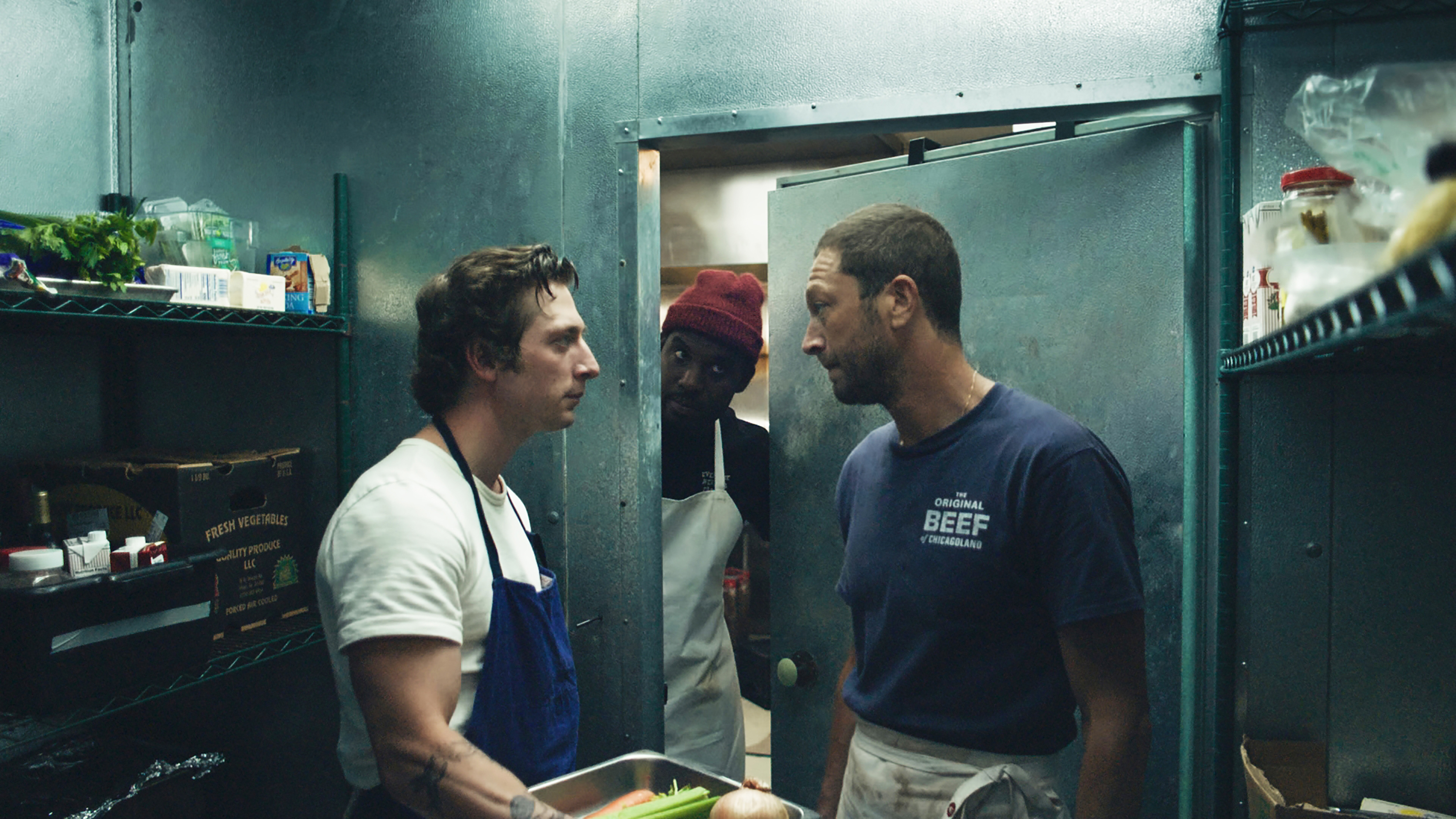 Two actors dressed as chefs square off in a kitchen.