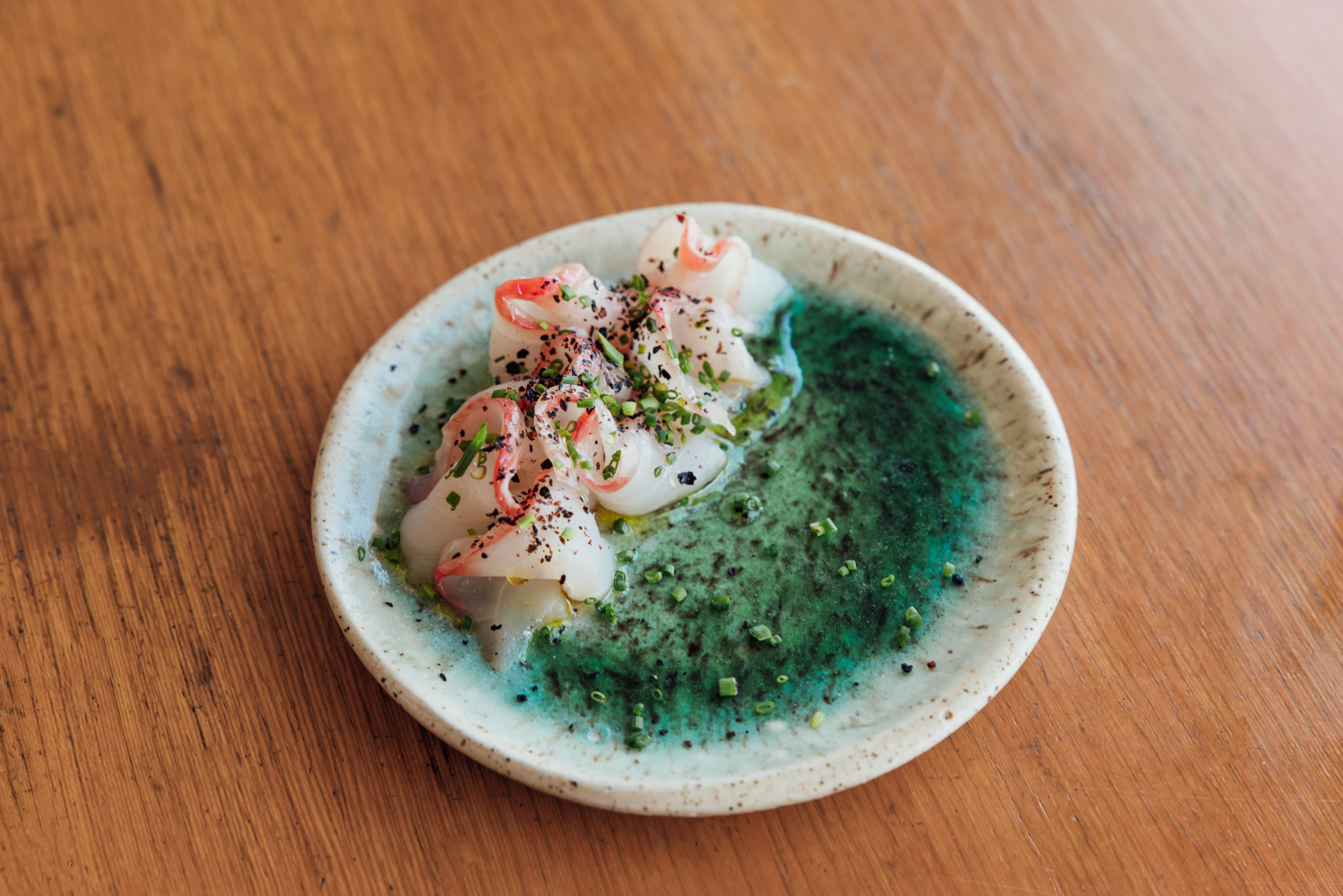 A plate of rockfish in vibrant green sauce and garnished with chives and chile.