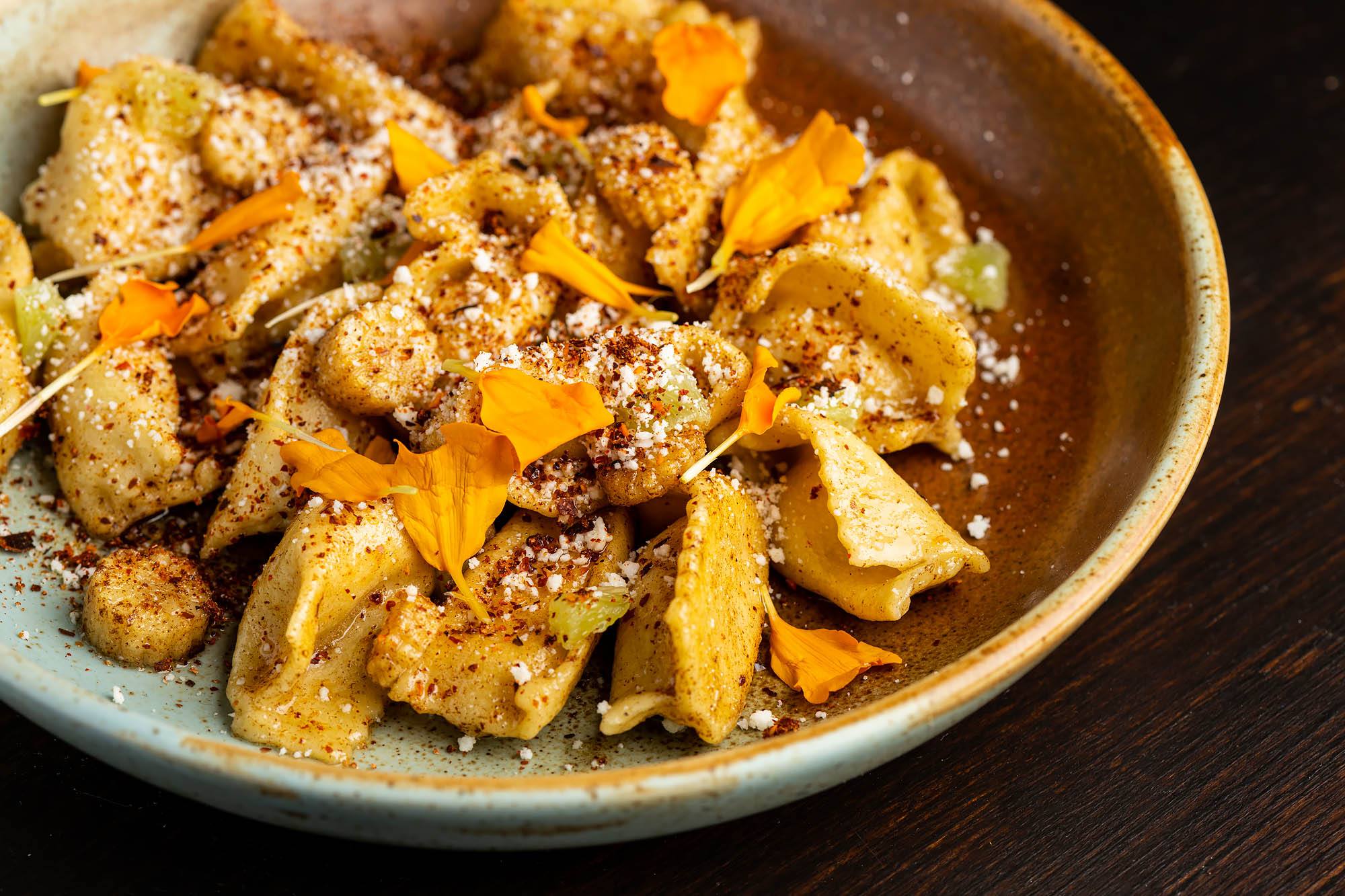 Yellow-orange stuffed pasta with edible flowers in a bowl.