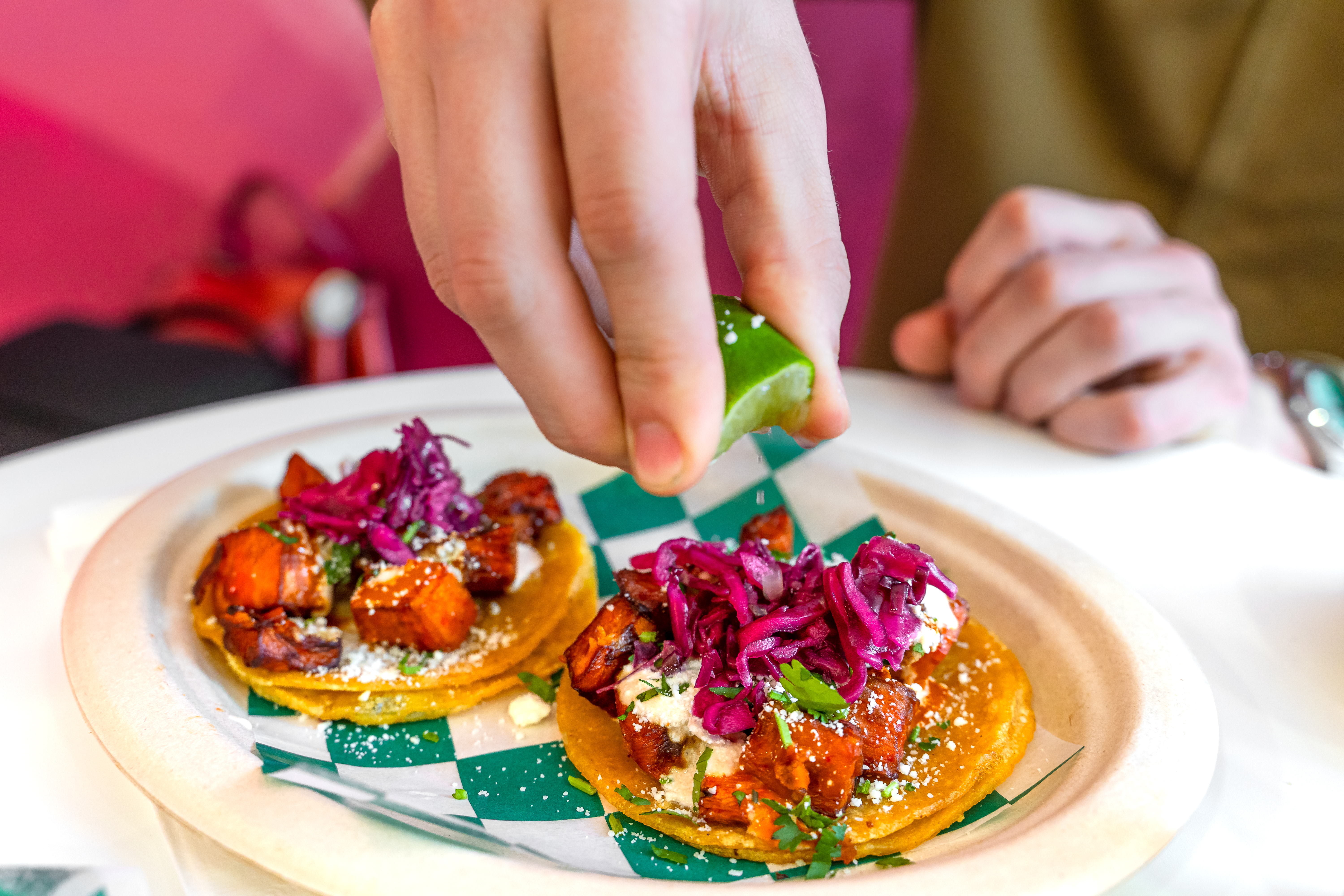 A hand squeezes a lime into a plate of two sweet potato tacos.