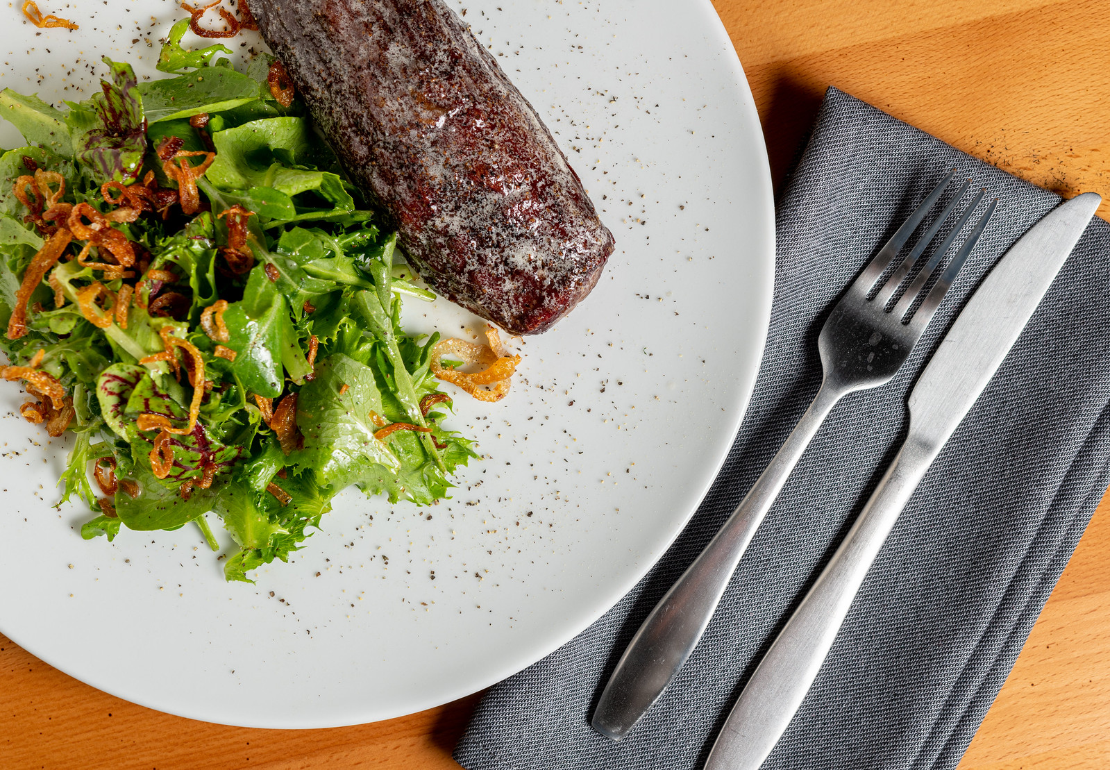 A strip steak on a plate next to a green salad.