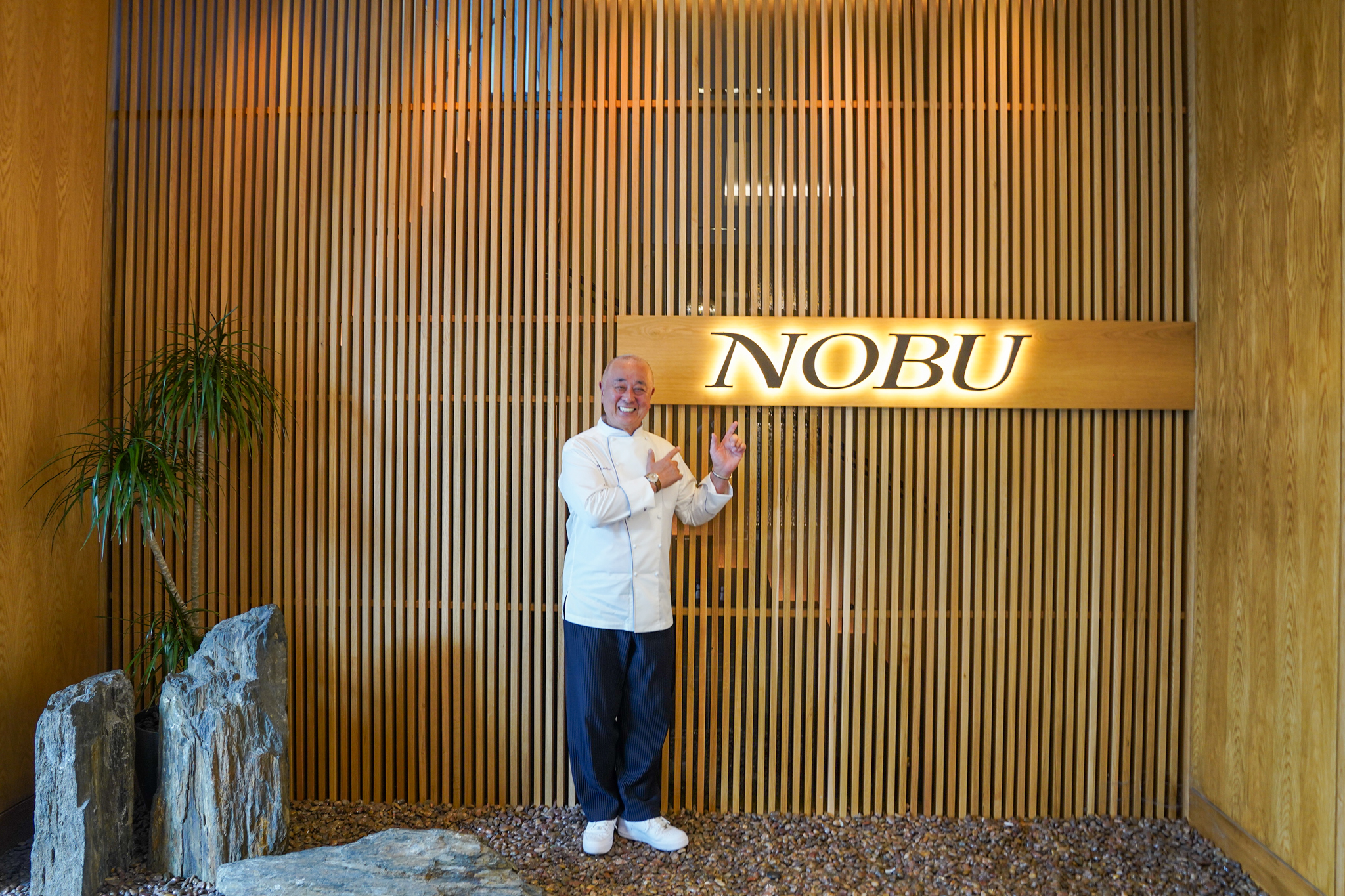Chef Nobu Matsuhisa points to illuminated Nobu sign at the Galleria Houston location.