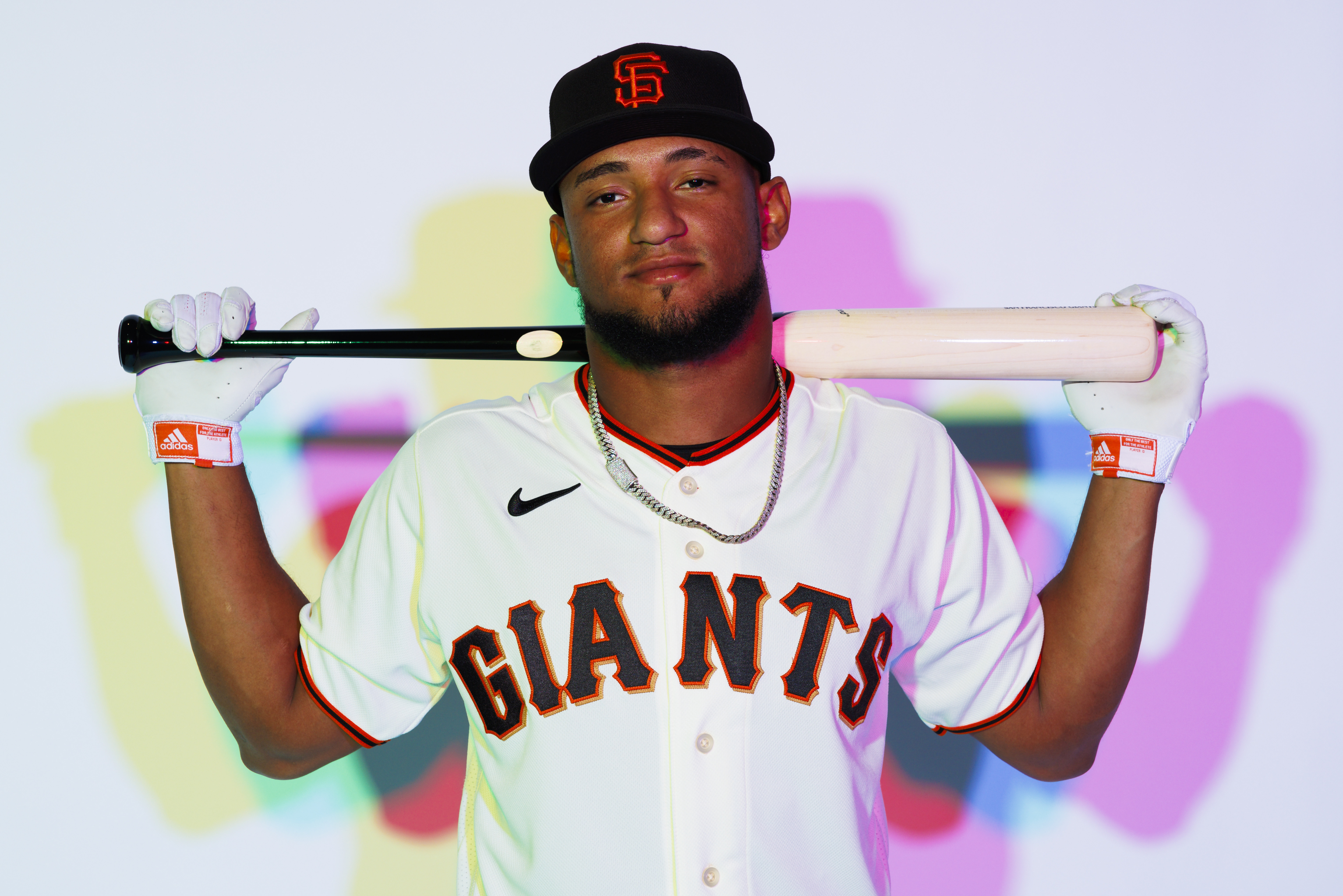 Luis Matos with the bat over his shoulders, posing in front of pastel colors at Giants media day.