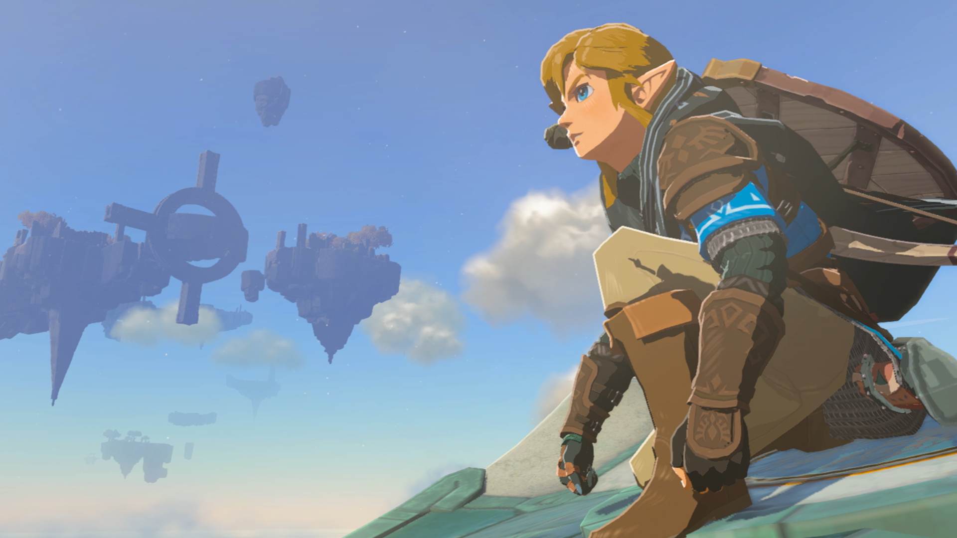An image of Link soaring through the sky on a Zonai glider. He’s crouching and a big blue sky filled with floating islands is in the background.